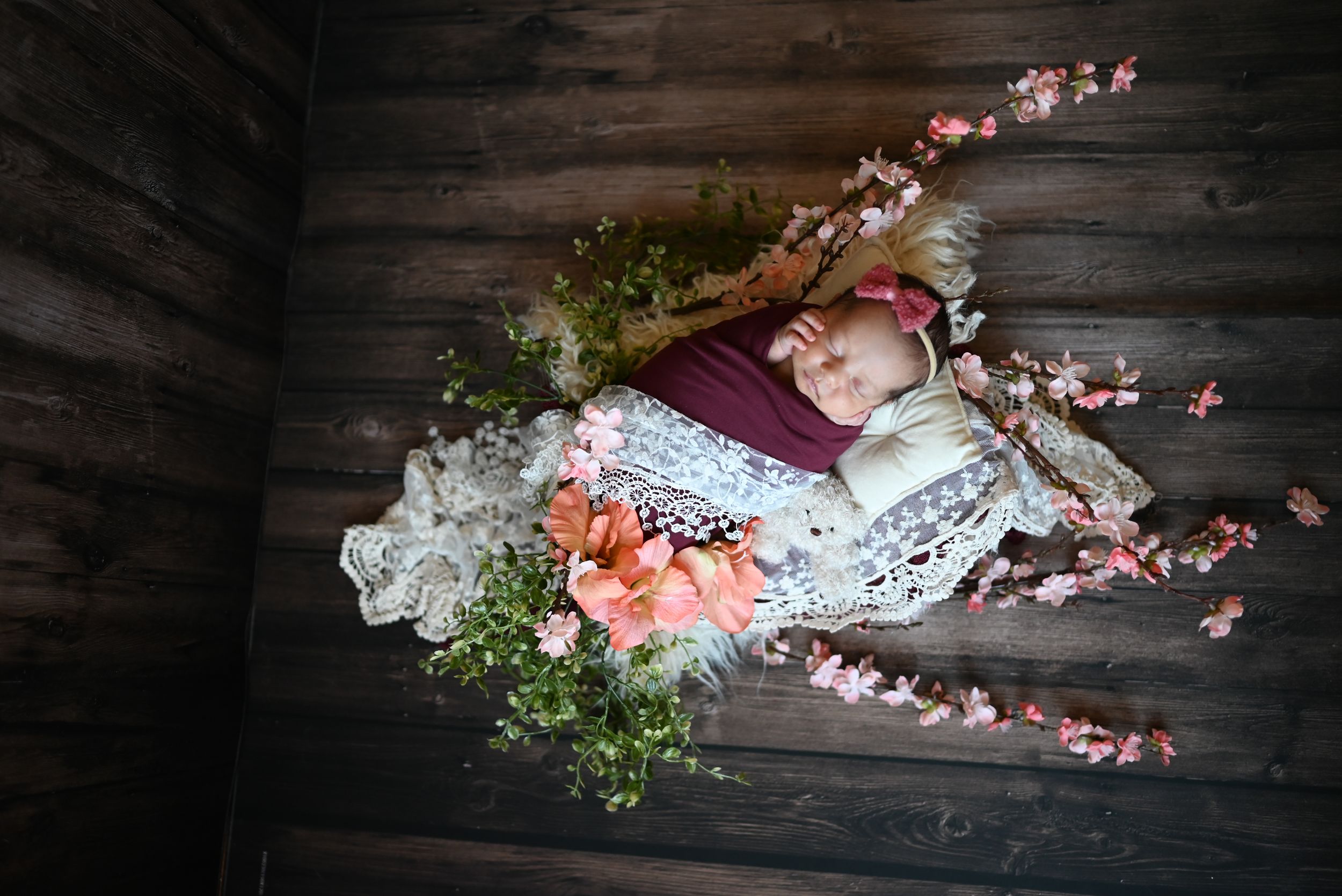 Pink cherry blossoms with vintage lace and delicate greenery arranged on dark rustic wooden backdrop.