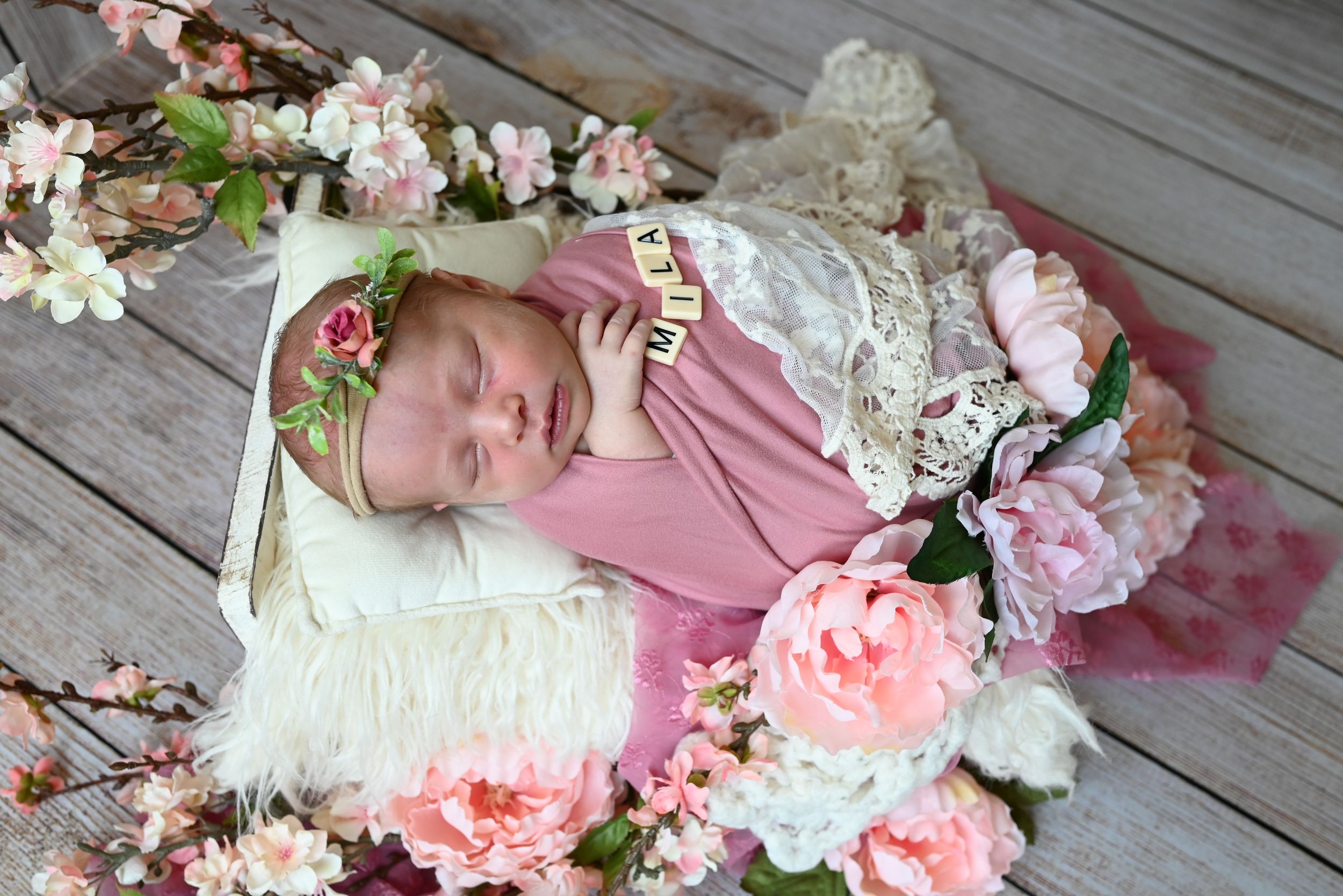 Sweet newborn photography setup with pink roses and white lace on rustic wooden floor.