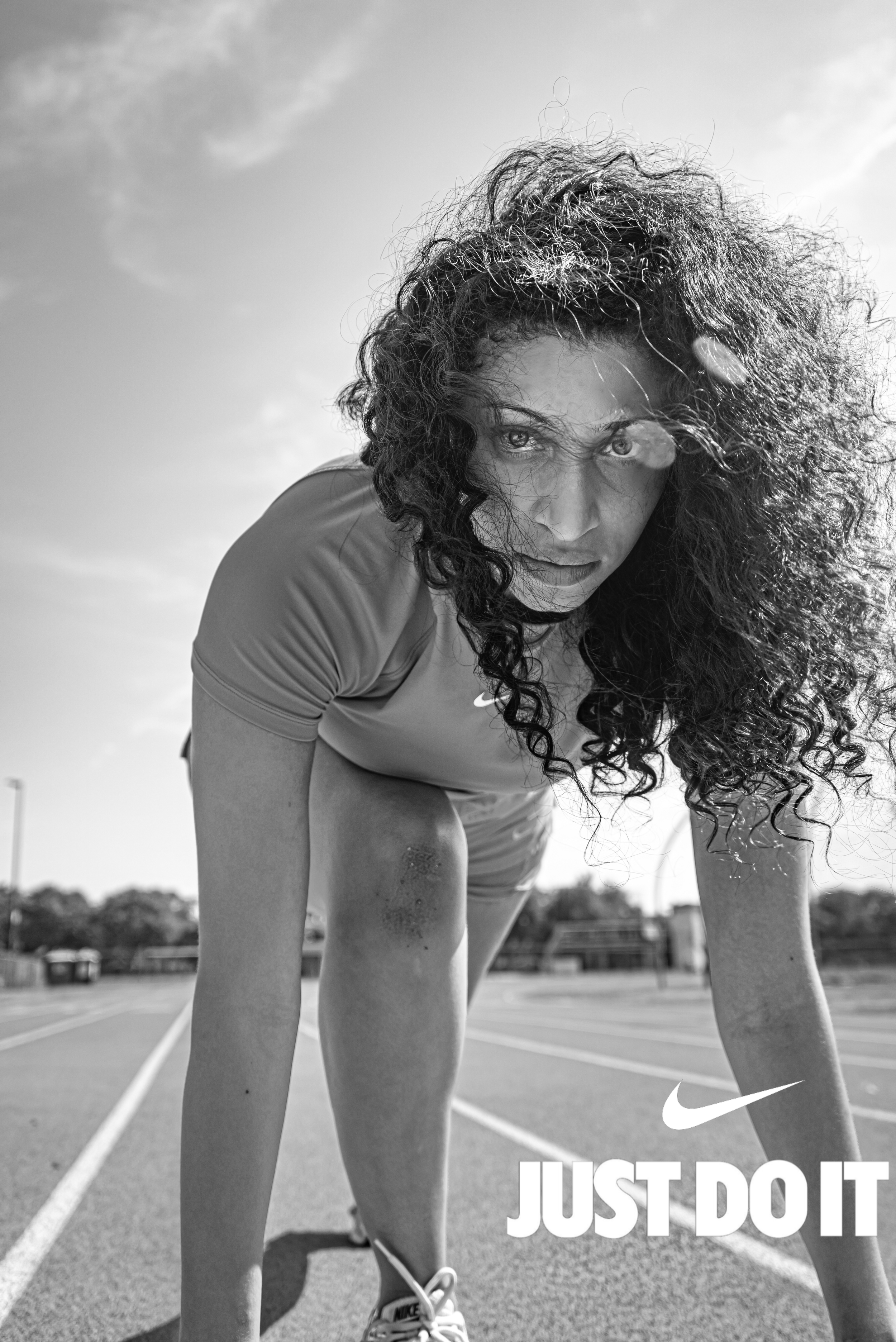 Black and white Nike advertisement showing athlete in starting position on a running track with Just Do It slogan.