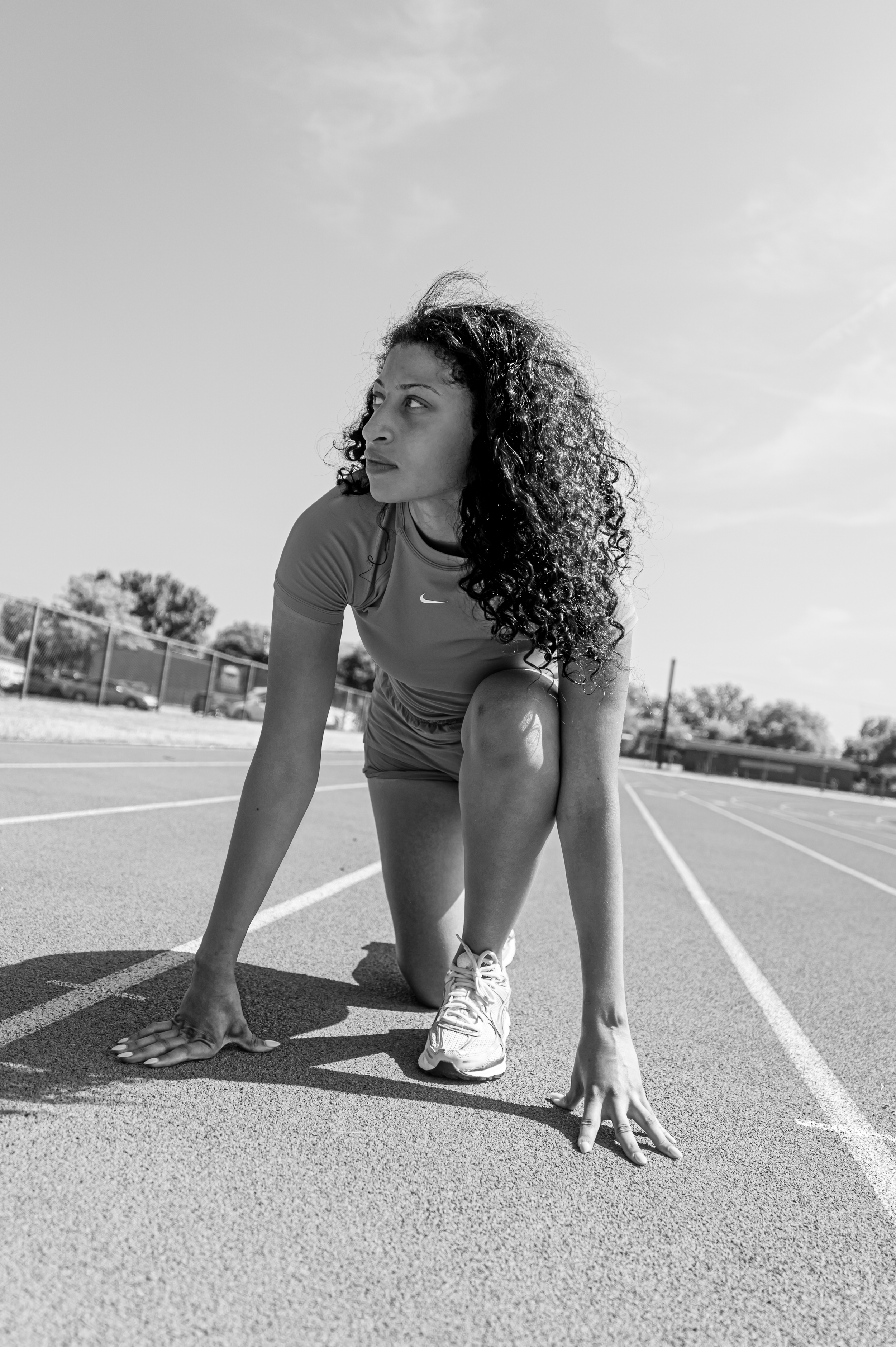 Black and white panoramic sequence shows an athlete in the ready position on a running track preparing to sprint.