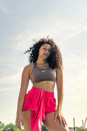 Athletic person in a gray Nike sports bra and bright red shorts poses outdoors during golden hour.