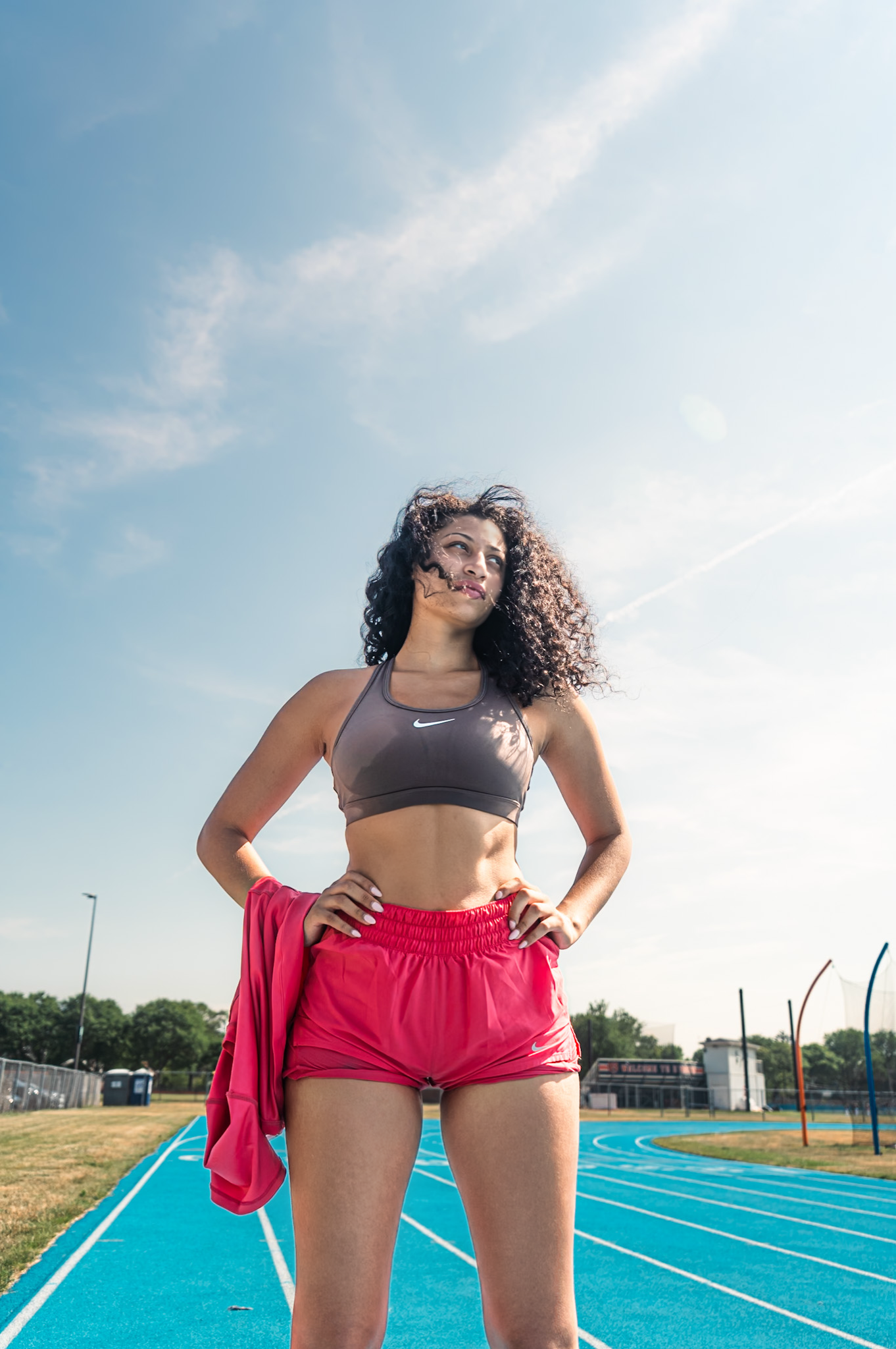 Athletic person in workout attire stands confidently on blue running track on sunny day.
