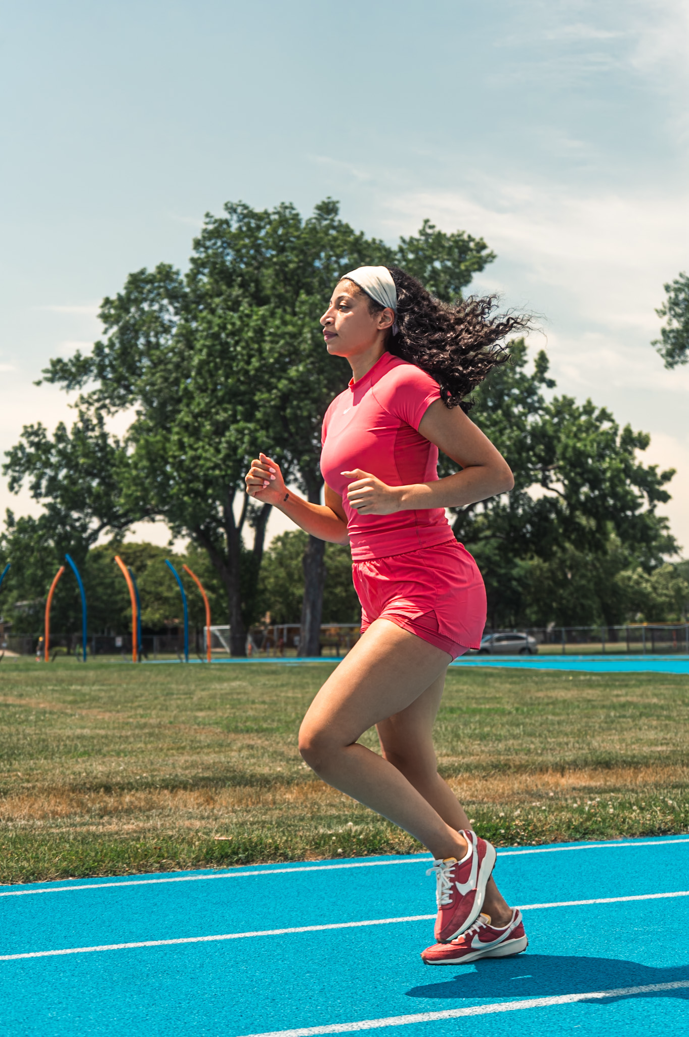 Runner in bright pink athletic wear sprints along vibrant blue running track on sunny summer day.