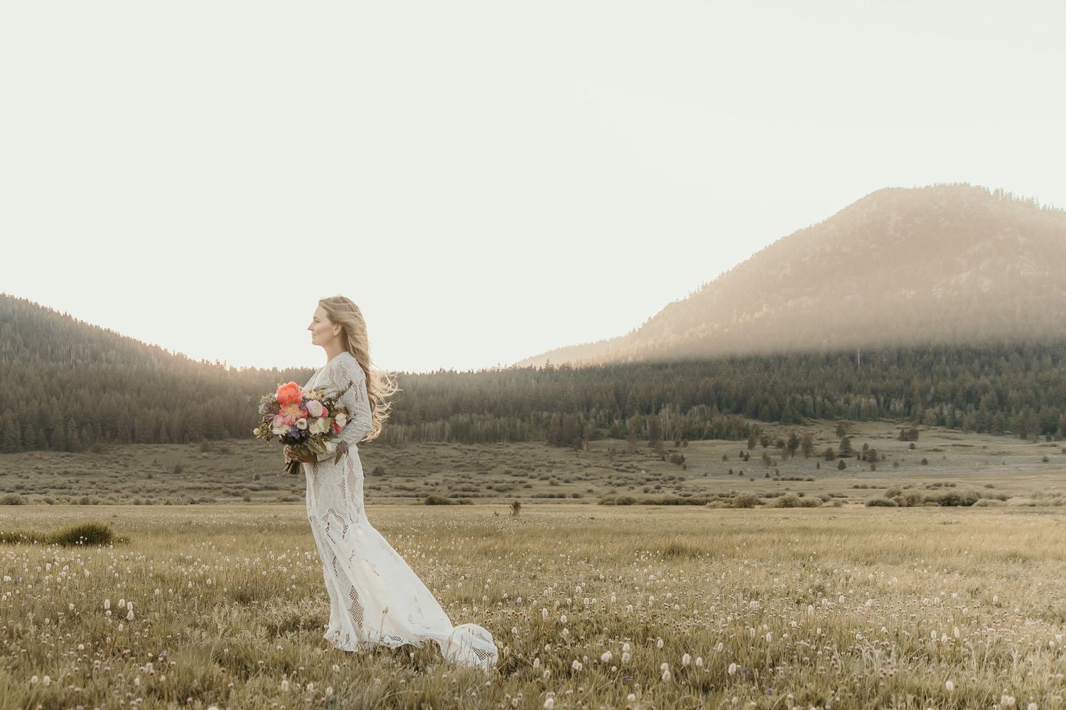 Scenic panorama of a couple in a vast mountainous meadow at sunset with wildflowers dotting the landscape.