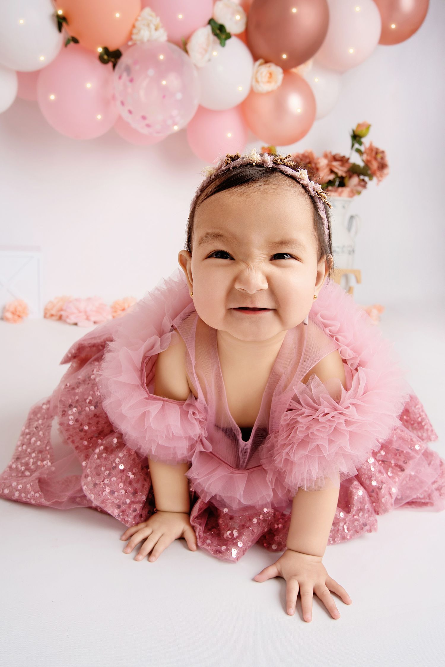 Baby photography with pink tulle dress and balloon decorations in soft pastel colors.