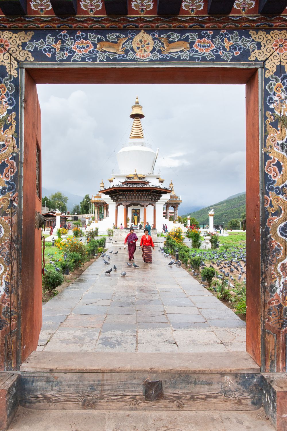 Ornate gateway frames white Buddhist stupa and temple path with decorative floral borders in Bhutan.
