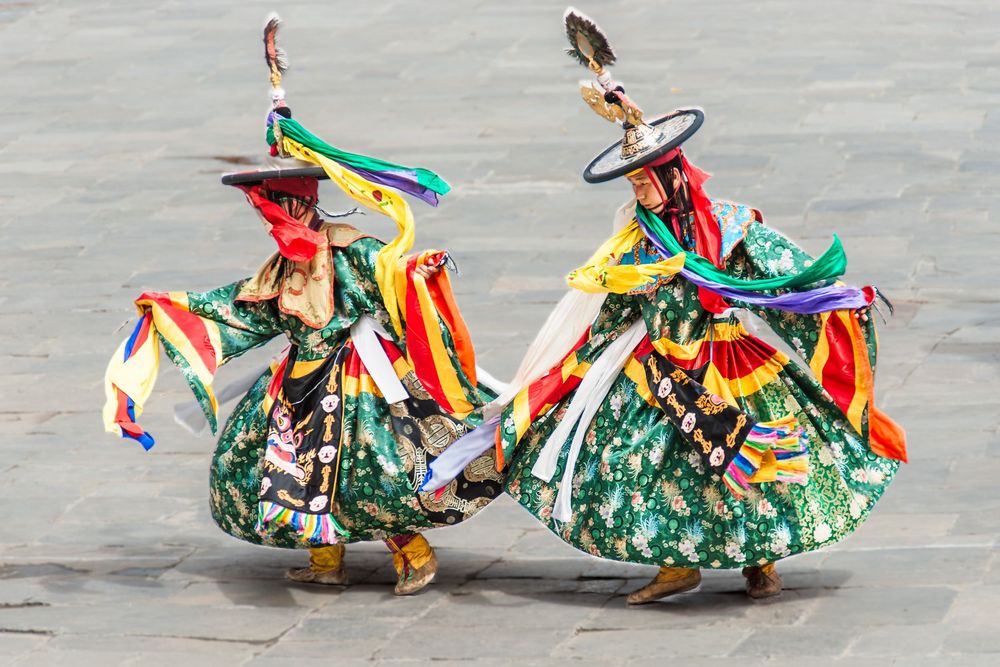 Traditional dancers perform in vibrant flowy costumes with colorful ribbons and green skirts during a cultural presentation.