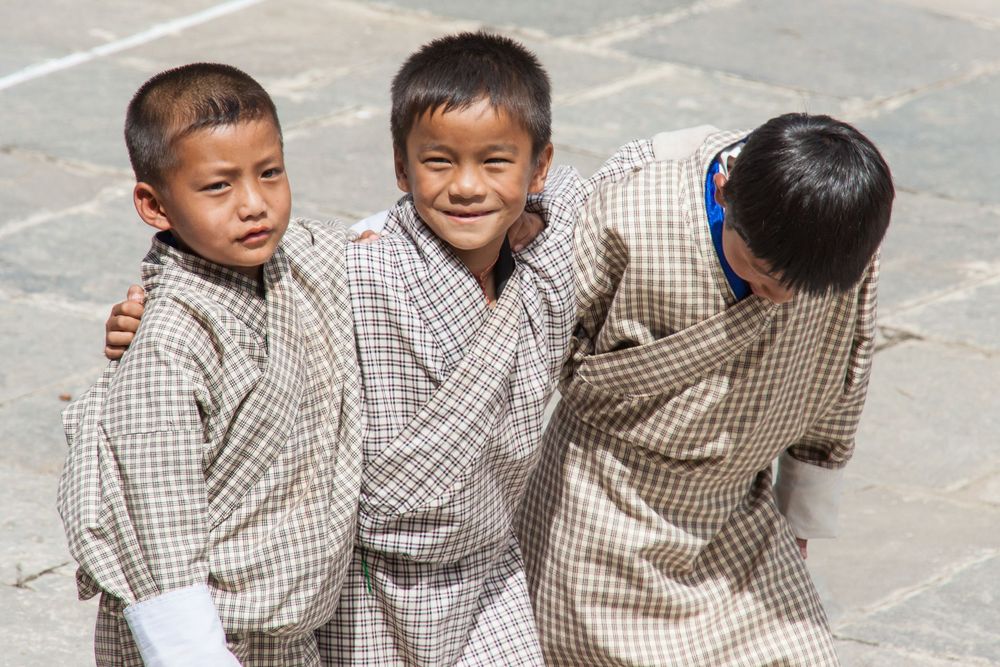 Three children in checkered shirts sit together and laugh on stone steps.