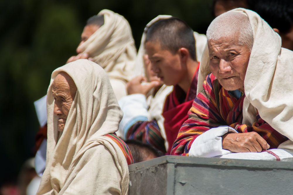 Elderly people in white and red clothing seated together at an outdoor gathering.