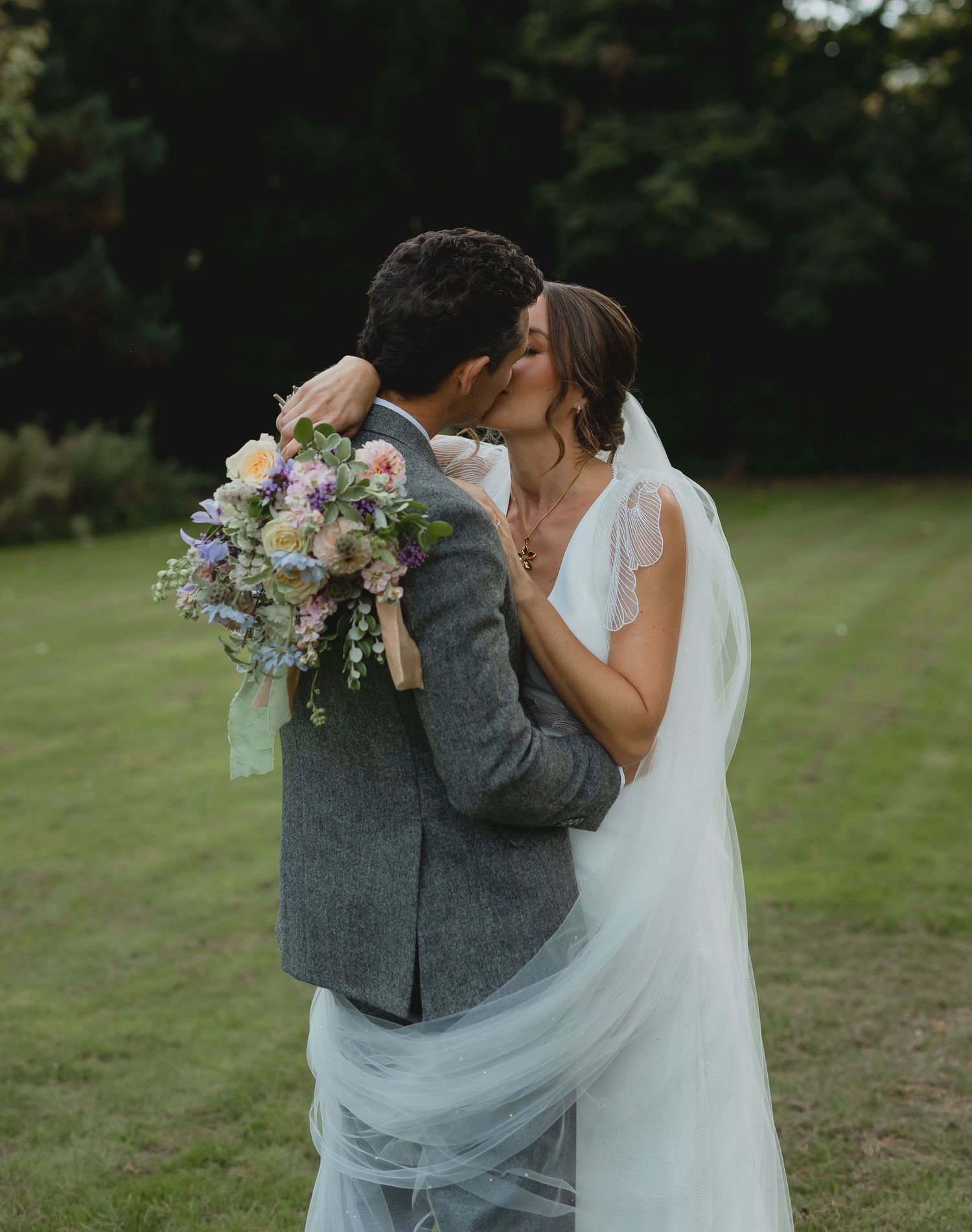 A couple shares their first kiss as newlyweds in an conservatory patio while guests look on with joy.