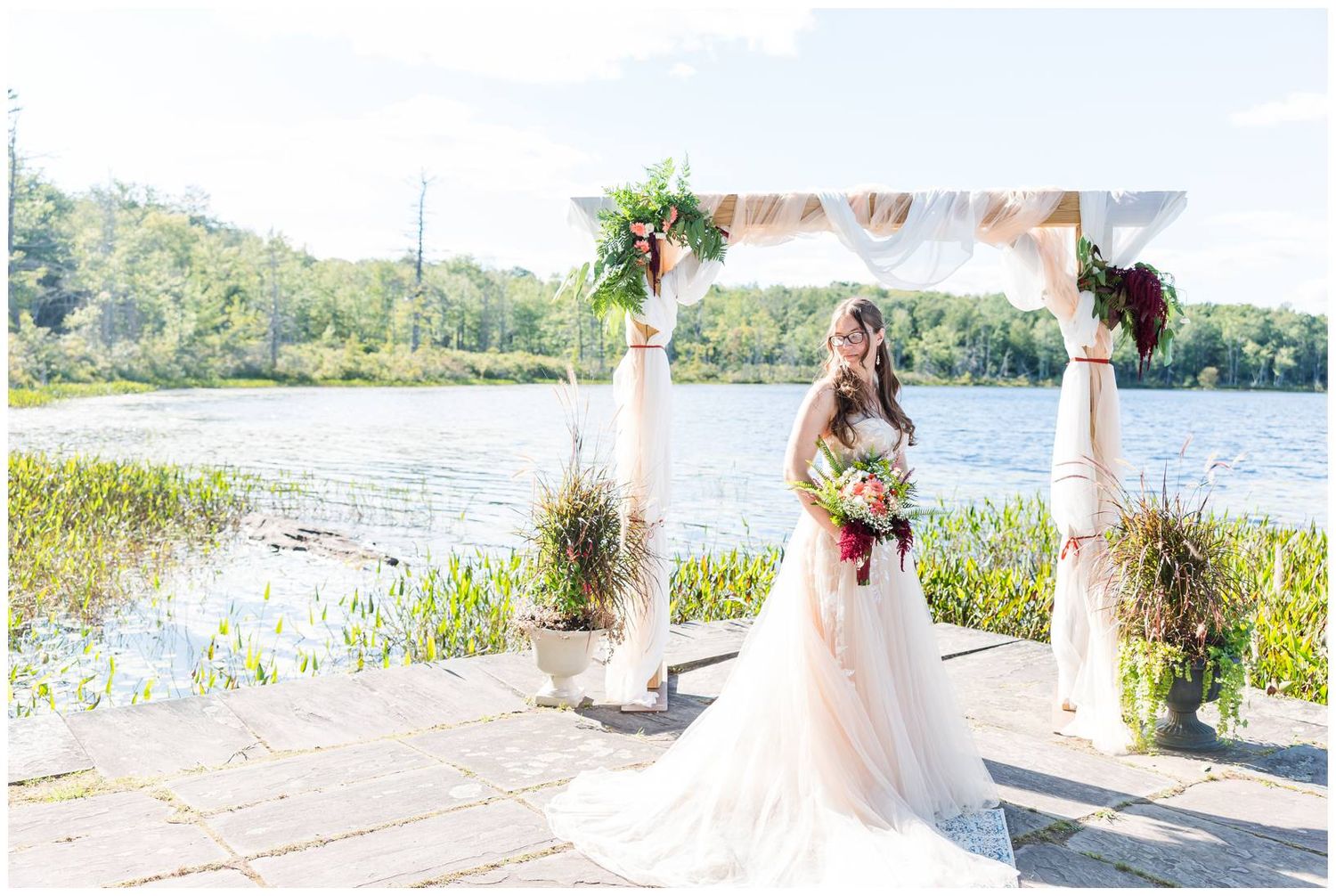 Intimate lakeside wedding ceremony with white arch and floral decorations overlooking the water.