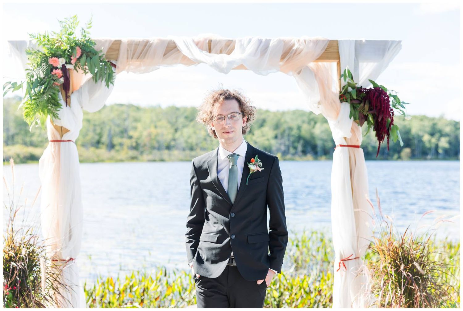 Elegant outdoor wedding ceremony setup by a lake with white draping and floral arrangements.