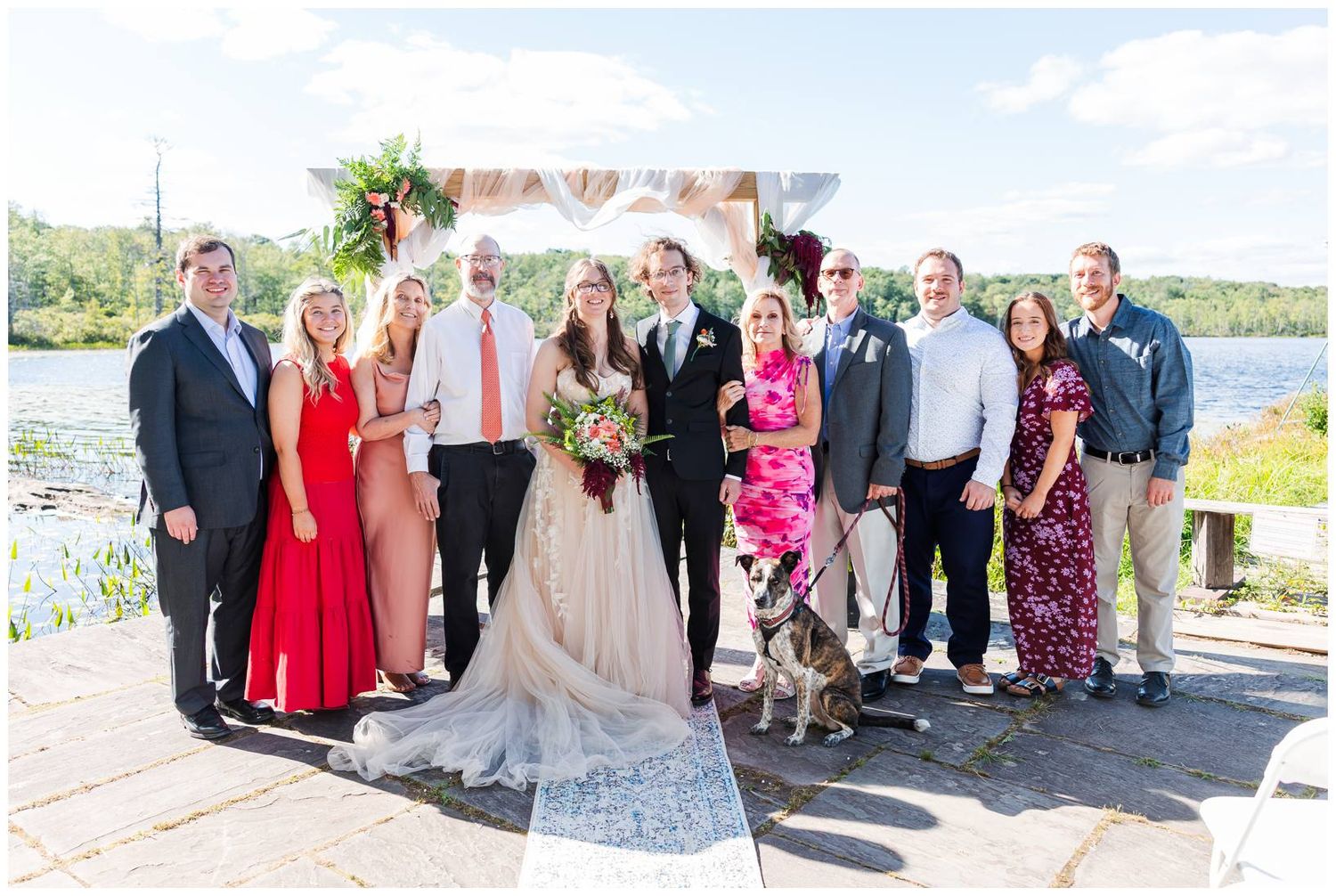 Wedding party group photos with guests lined up outdoors by a waterfront on a sunny day.