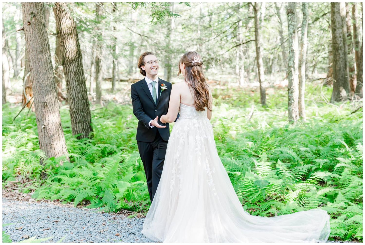 A wedding couple walks through a lush green forest setting with ferns and tall trees creating a natural backdrop.