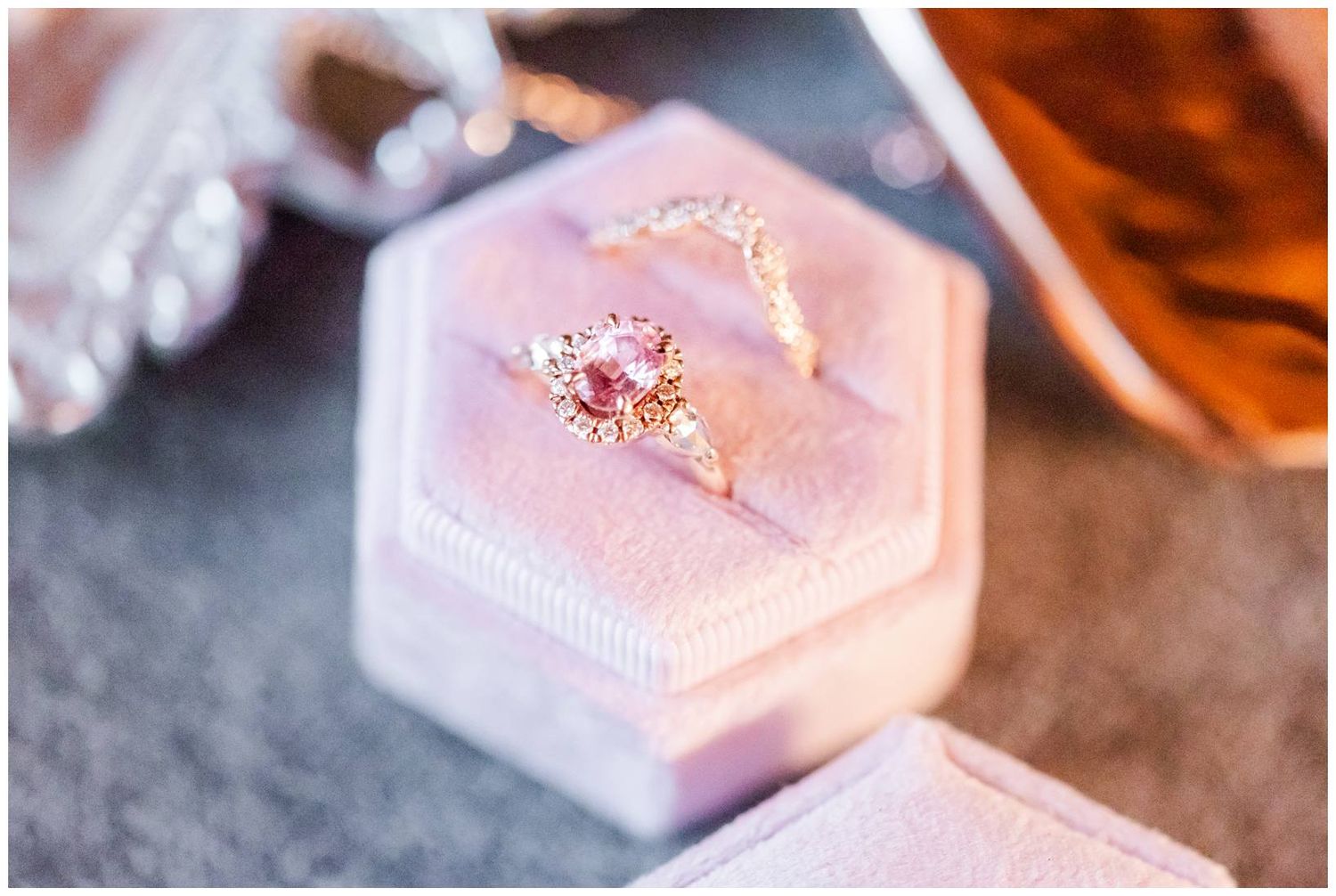 A delicate pink engagement ring in a pearly blush box glimmers in warm lighting from multiple angles.
