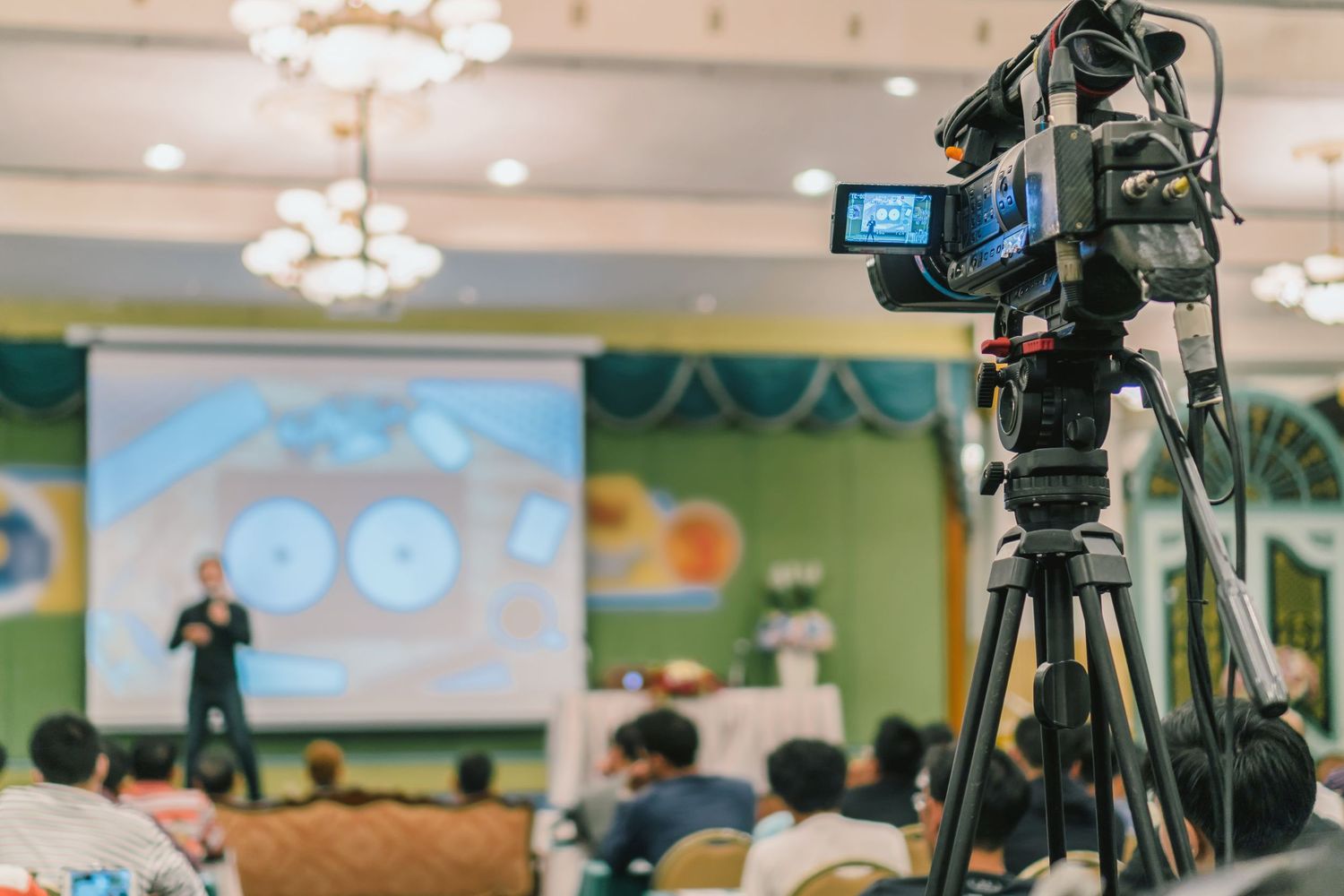 Professional video cameras and equipment set up in a conference room with chandeliers and colorful walls.