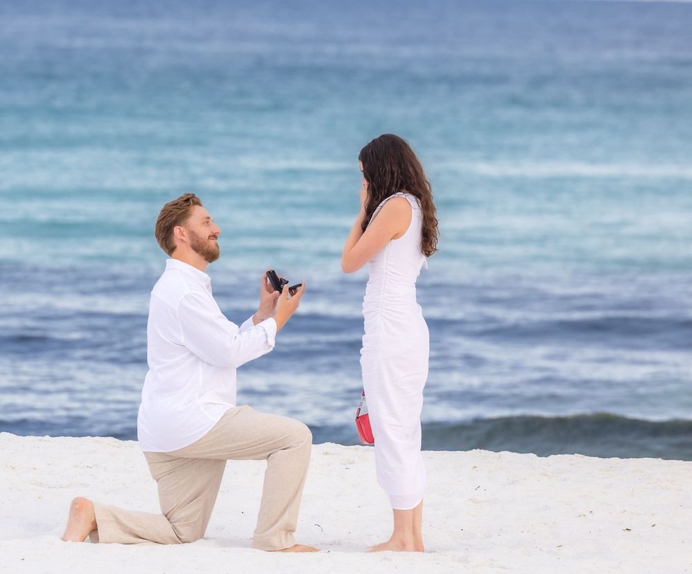A romantic beach proposal unfolds in a sequence of photos showing a couple in white outfits by the ocean at sunset.