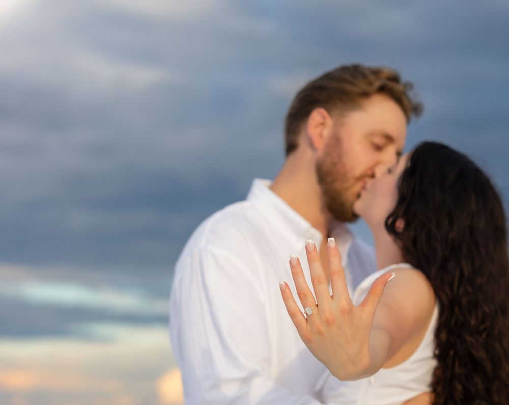A couple embracing and kissing on a beach at sunset with dramatic cloudy skies in the background.