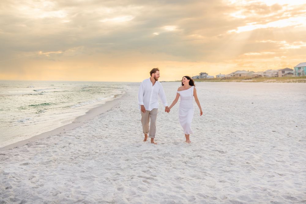 Couple walking hand in hand on a pristine white sandy beach at sunset with soft golden light in the background.