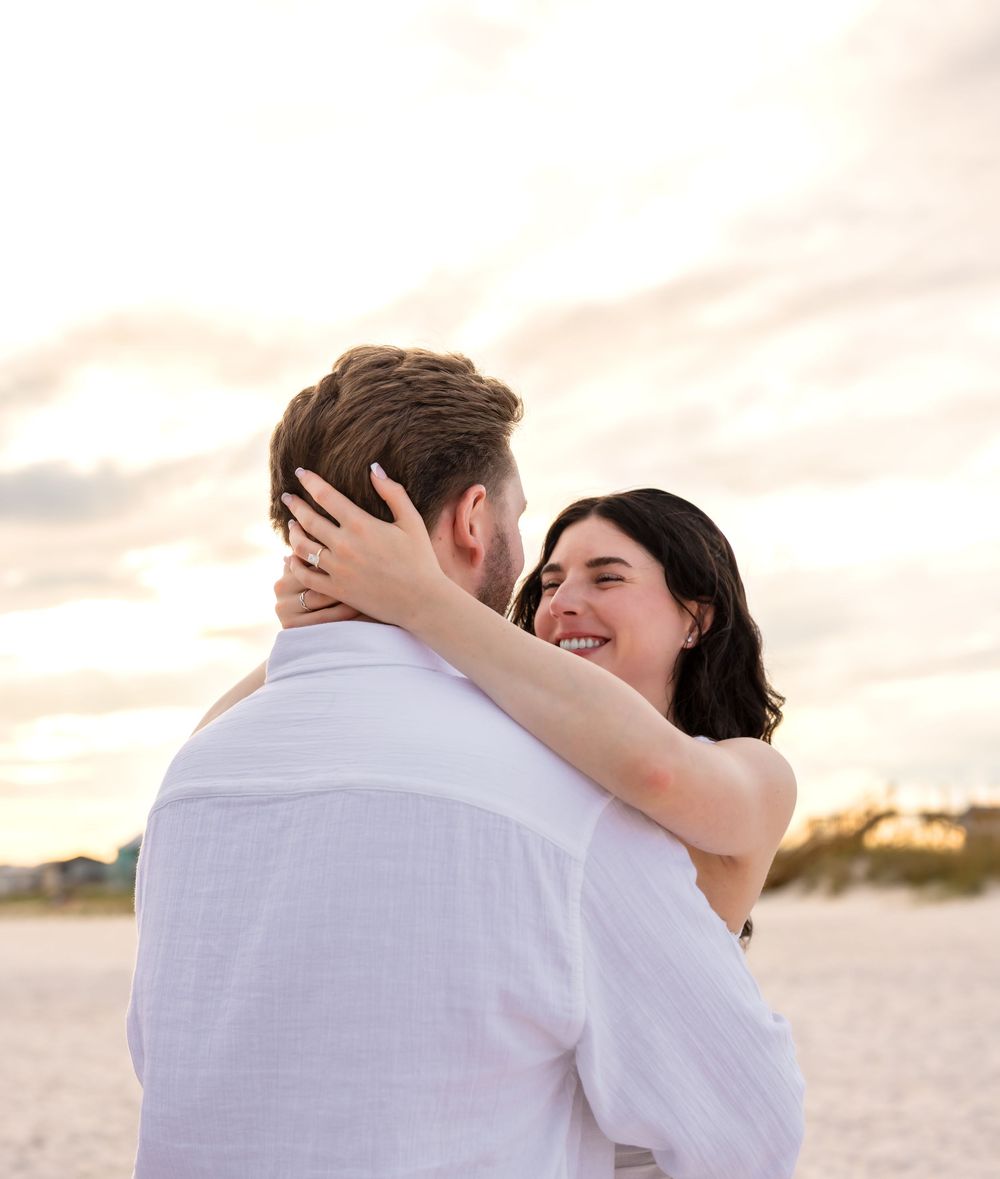 Two people embracing on a sandy beach at sunset in a romantic moment by the ocean.