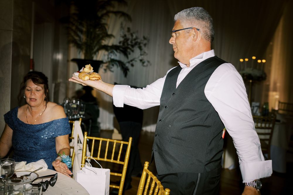 Wedding guests dancing and enjoying themselves at an elegant reception with gold chairs and ambient lighting.