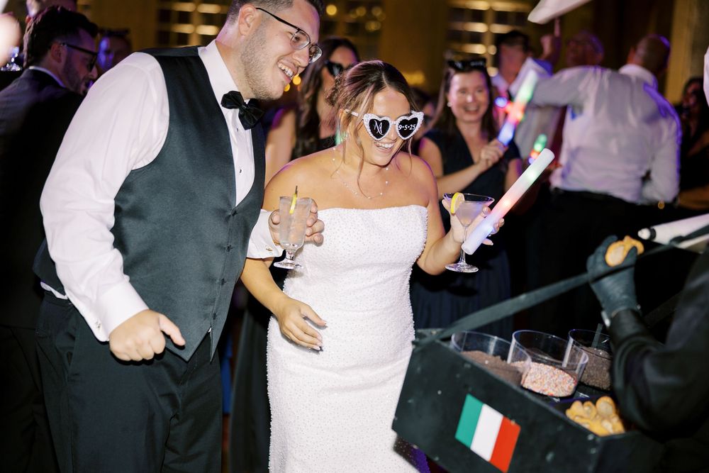 Wedding guests dance and celebrate during a lively reception party with people holding small flags on the dance floor.