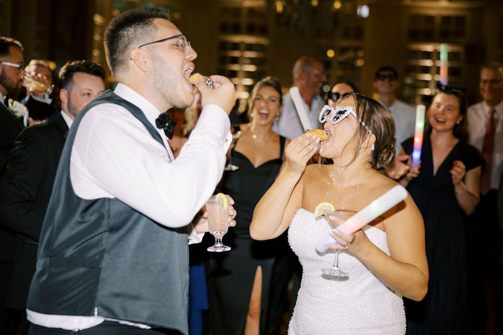 People dancing and celebrating at an indoor wedding reception with festive lighting and joyful atmosphere.