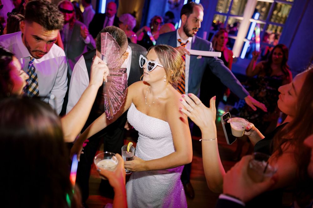 Dance party celebration at wedding reception with heart-shaped sunglasses and colorful lighting effects.
