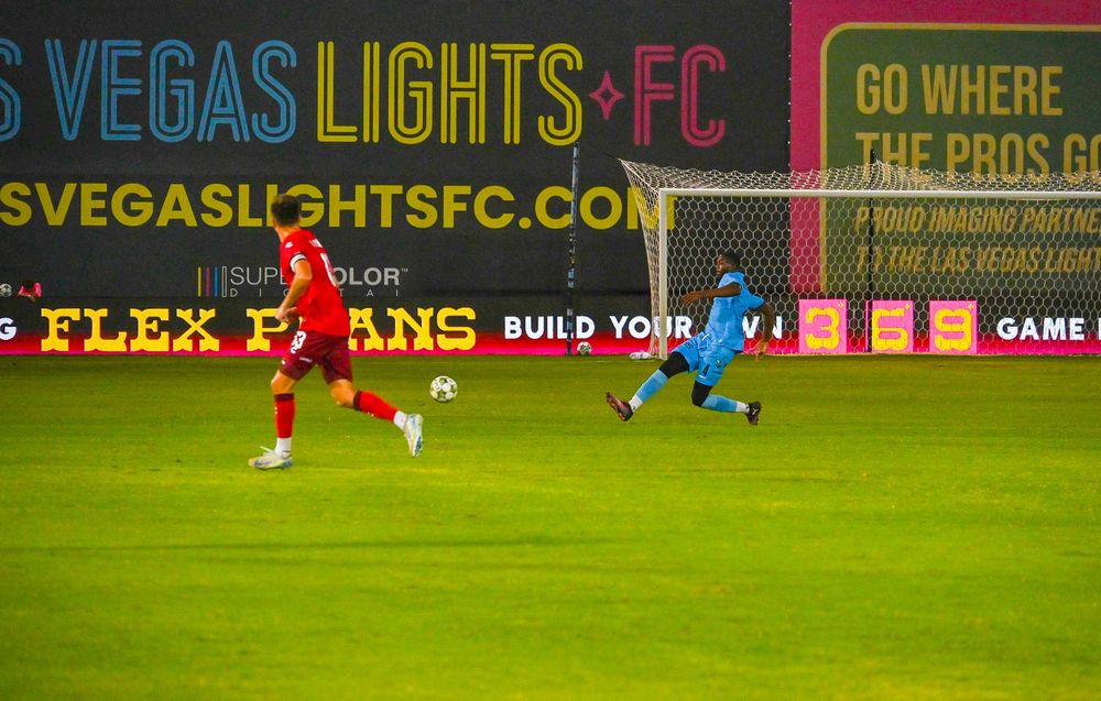 Two soccer players compete on the field in front of Vegas Lights FC stadium signage.