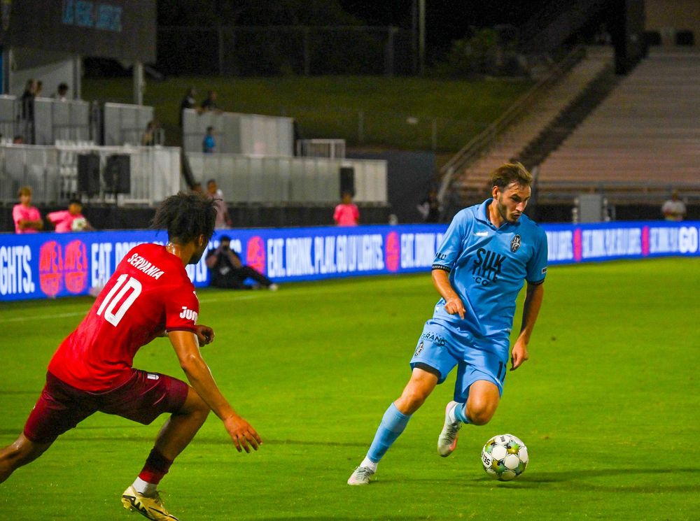 Las Vegas Lights FC player in blue dribbles past opponent wearing number 10 jersey during night match.