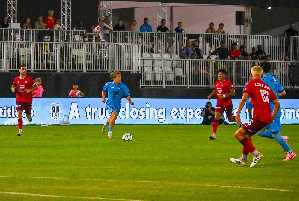 Las Vegas Lights FC players in blue jerseys compete against red-uniformed opponents during a night soccer match.