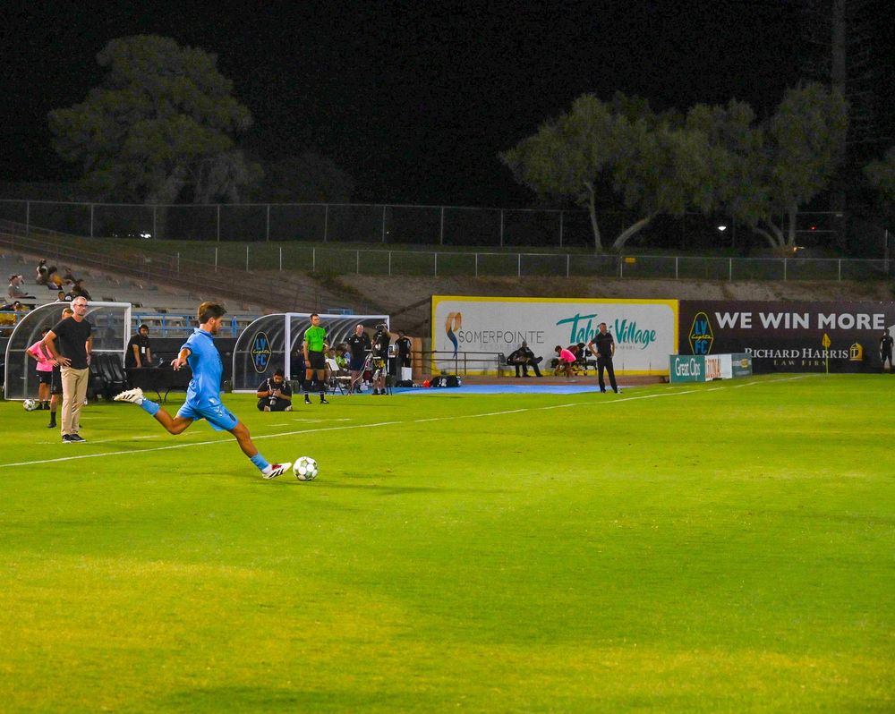 Soccer player in blue jersey taking a kick during a night game at a professional stadium.