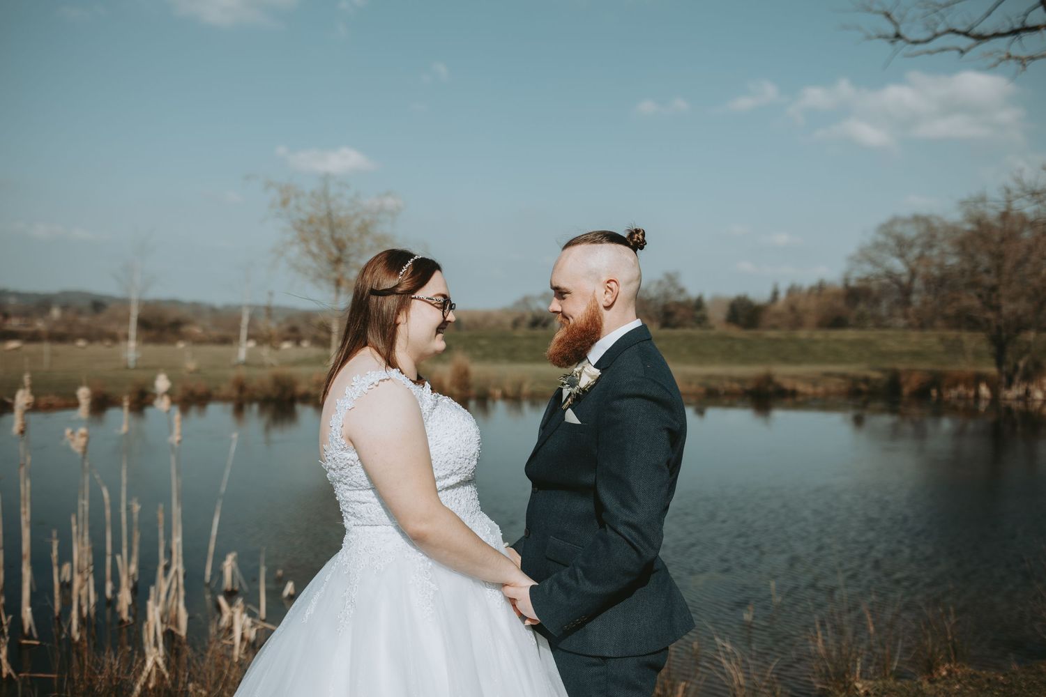 A romantic outdoor wedding portrait session with a couple near a lake and bare winter trees in the background.