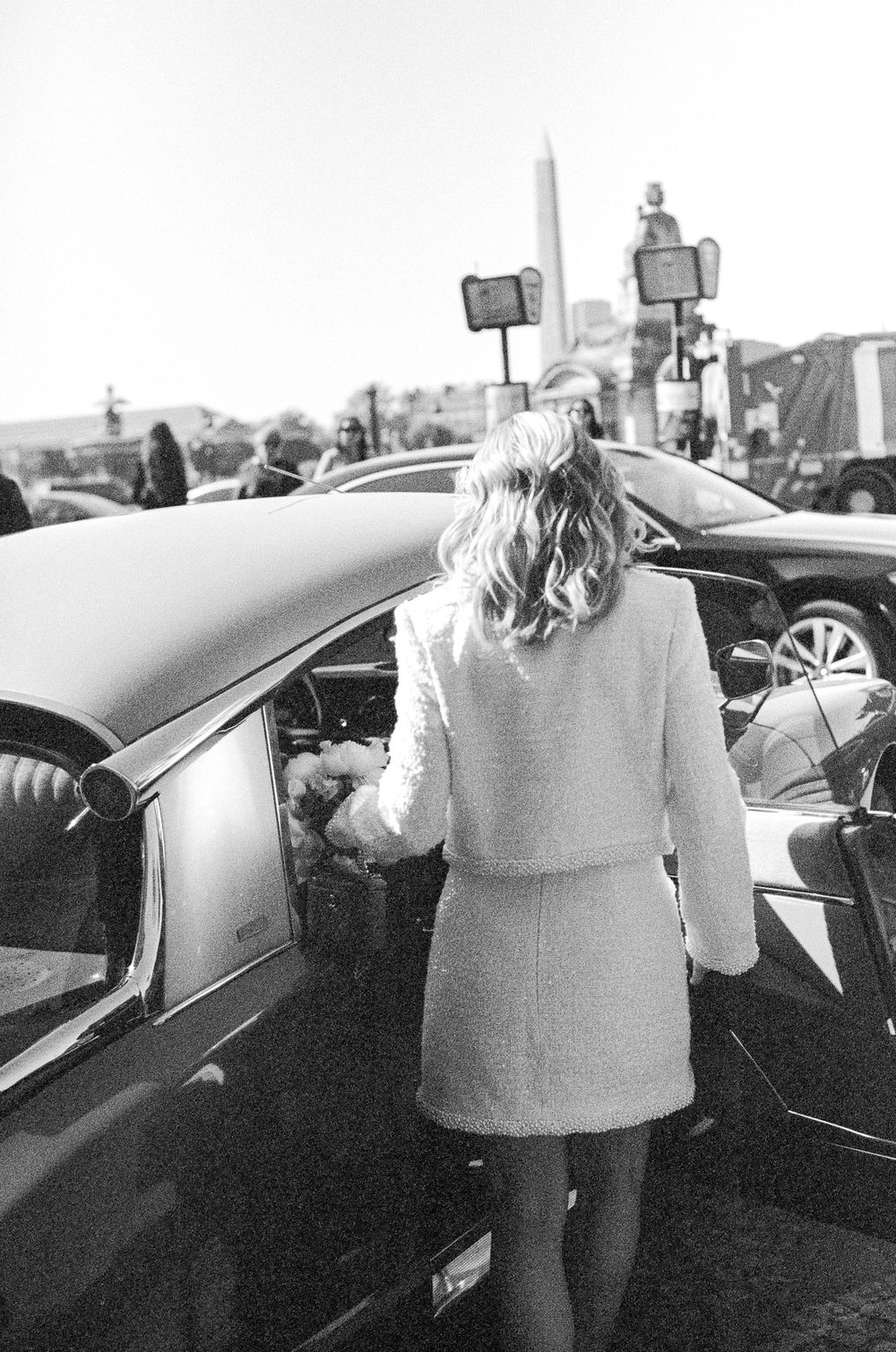 A person in light-colored clothing stands next to a car in a sequence of four black and white photographs.