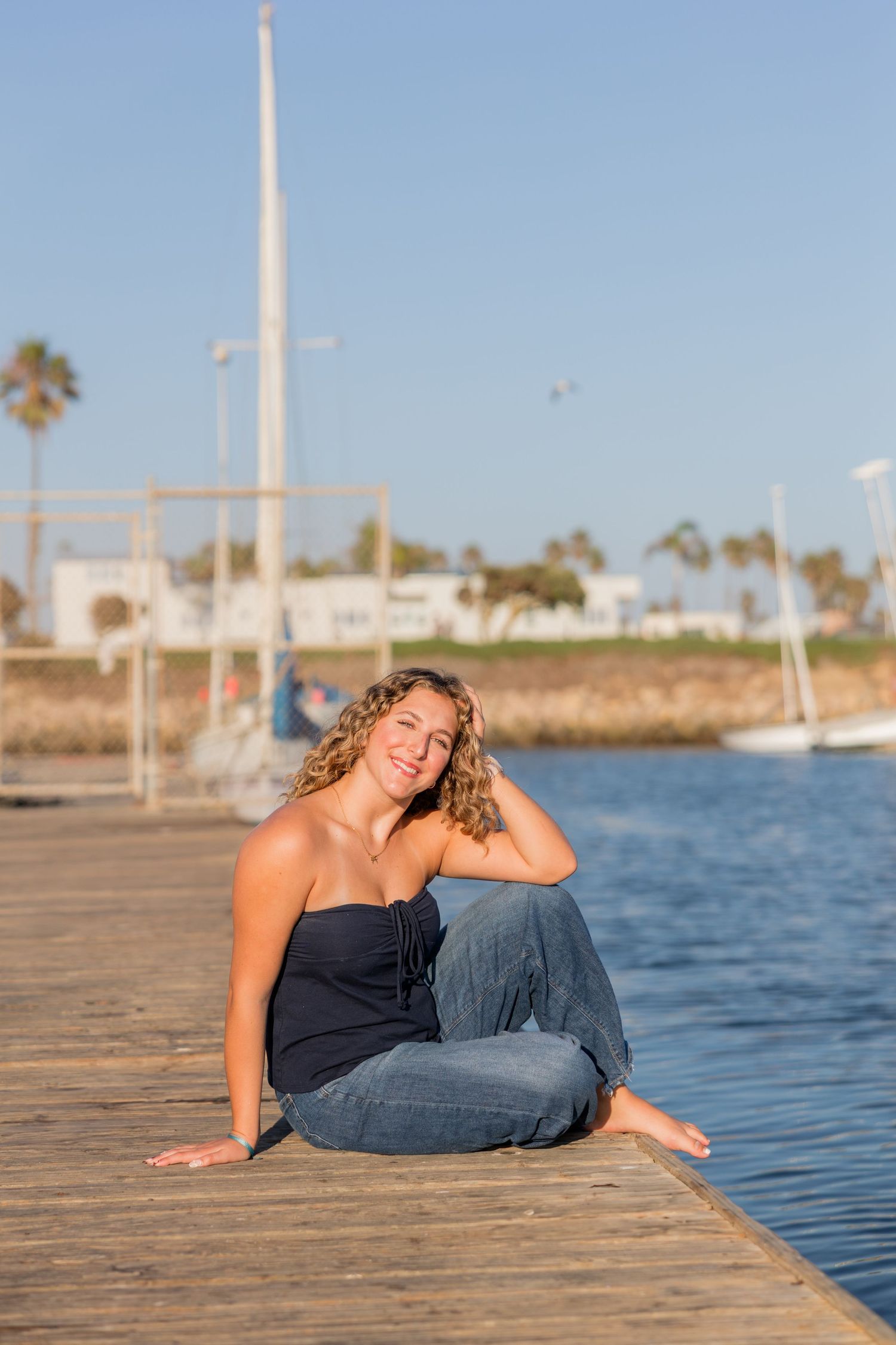 A person in casual attire relaxes on a wooden dock by the water on a sunny day.