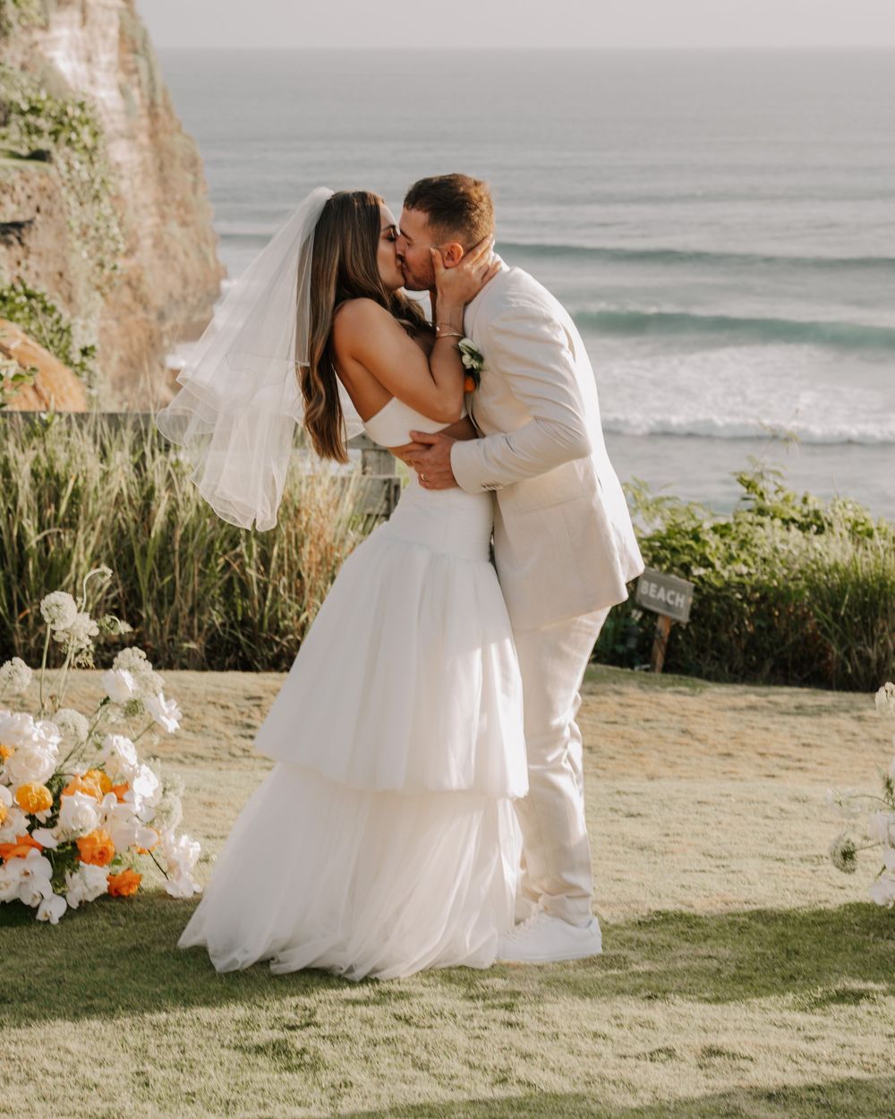 A romantic beach wedding scene with cliffs and ocean in the background as a couple shares a tender moment.