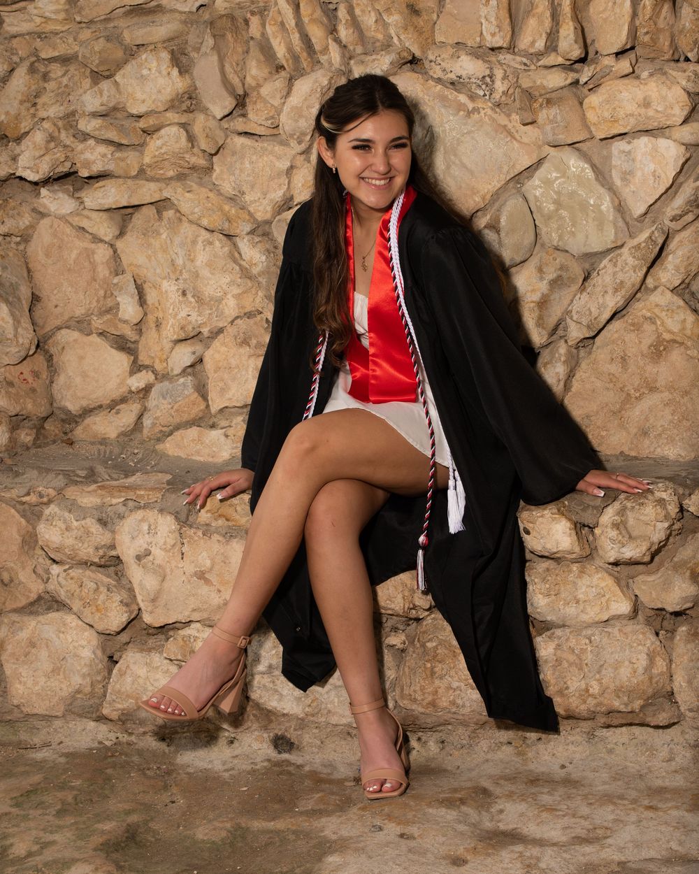 A stylish combination of a formal black coat and red dress is captured against a textured stone wall backdrop.