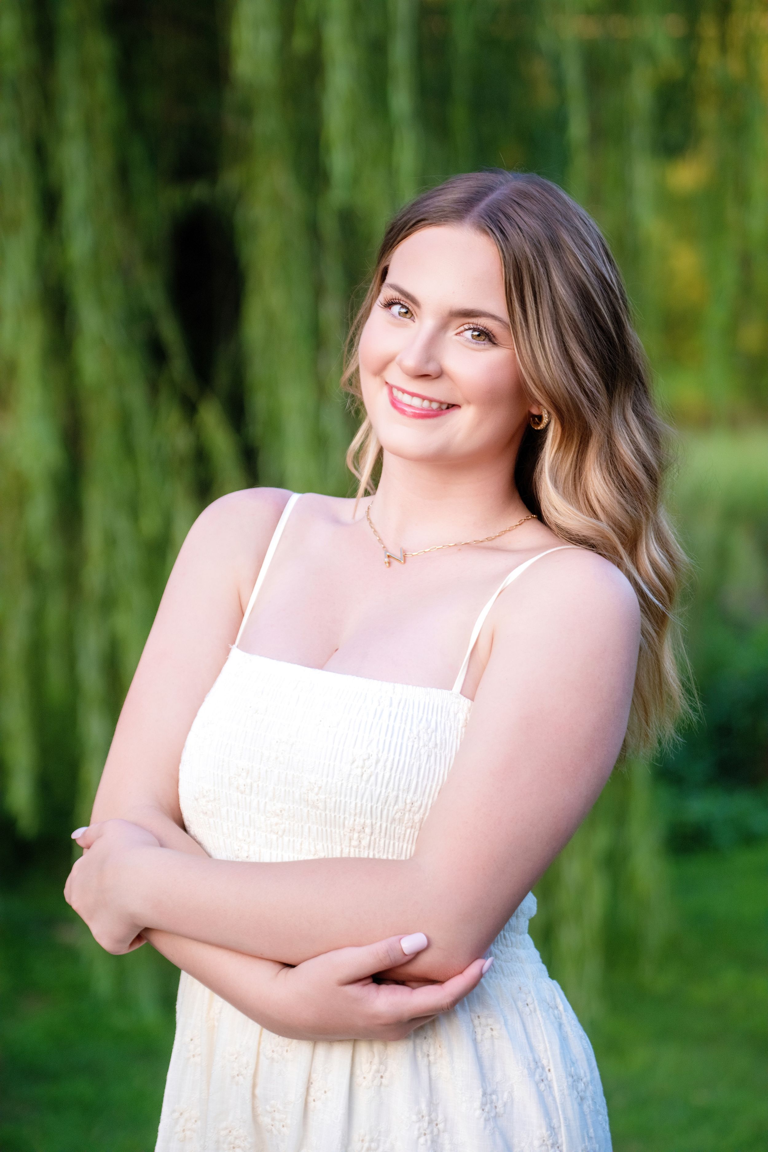 Portrait session in a white sundress against a soft green willow tree background on a sunny summer day.