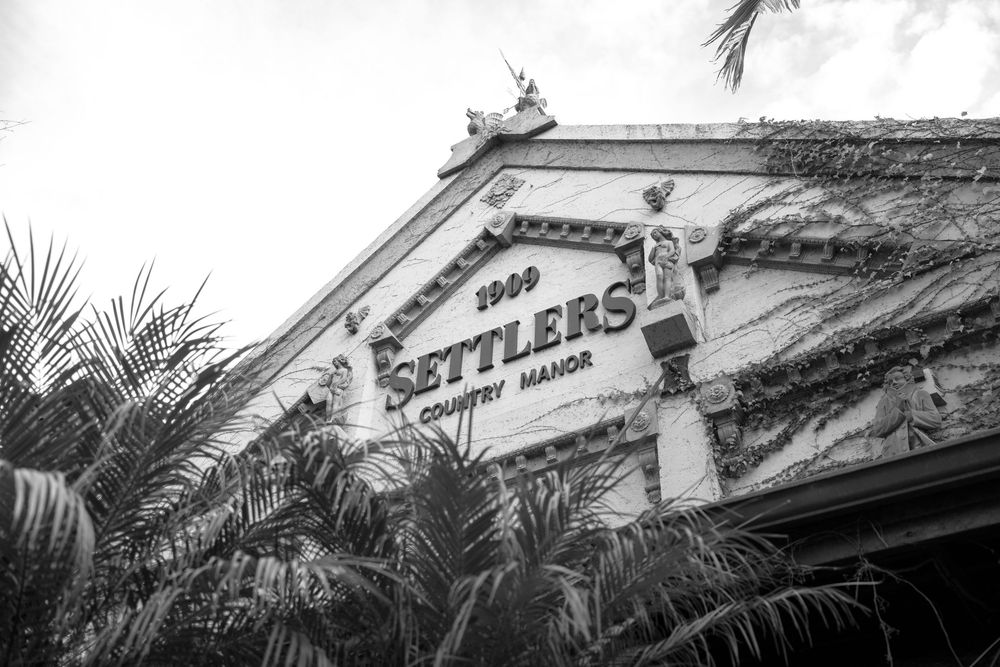 Black and white photo of Settlers Country Manor sign on a historic building facade with palm trees.