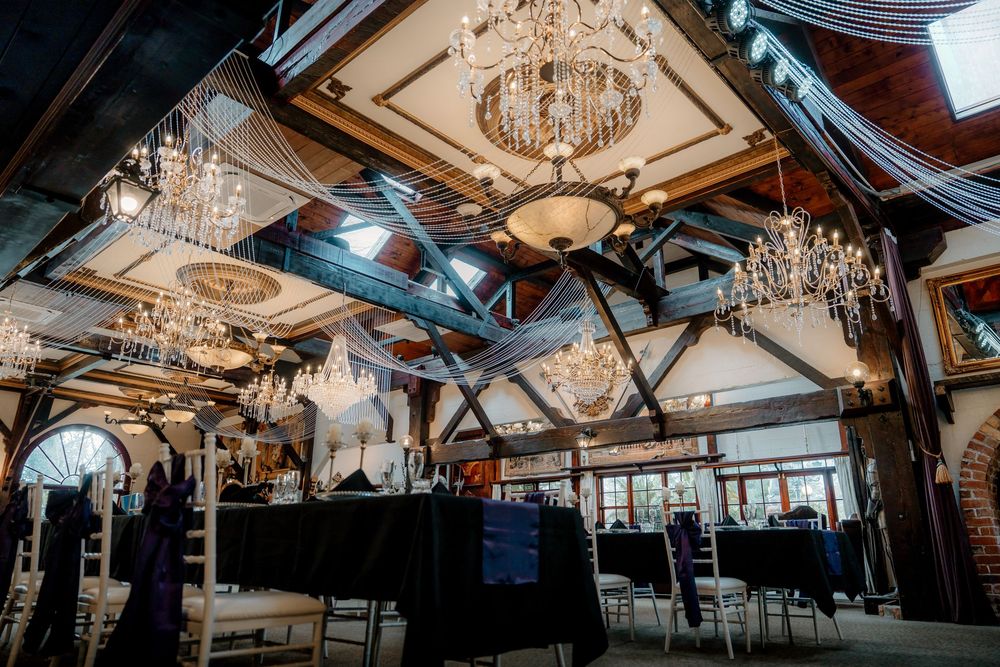 Elegant banquet hall with crystal chandeliers, dark ceiling beams, and black-draped tables set for a formal event.