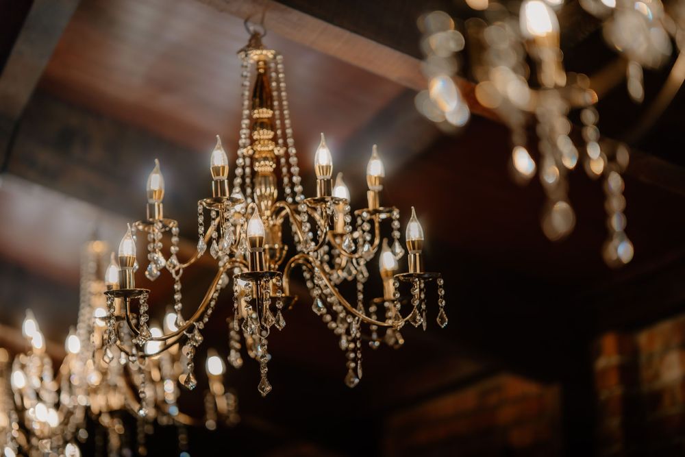 Elegant crystal chandelier with glowing candle-style lights hanging from a dark wooden ceiling in a luxurious interior.