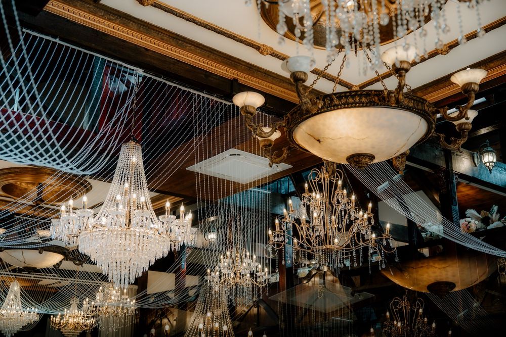 Elegant crystal chandeliers displayed in a luxurious showroom with ornate gold ceiling details.