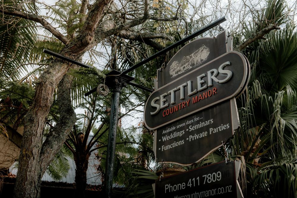 Settlers Country Manor sign surrounded by lush palm trees, offering weddings, seminars, and private parties.