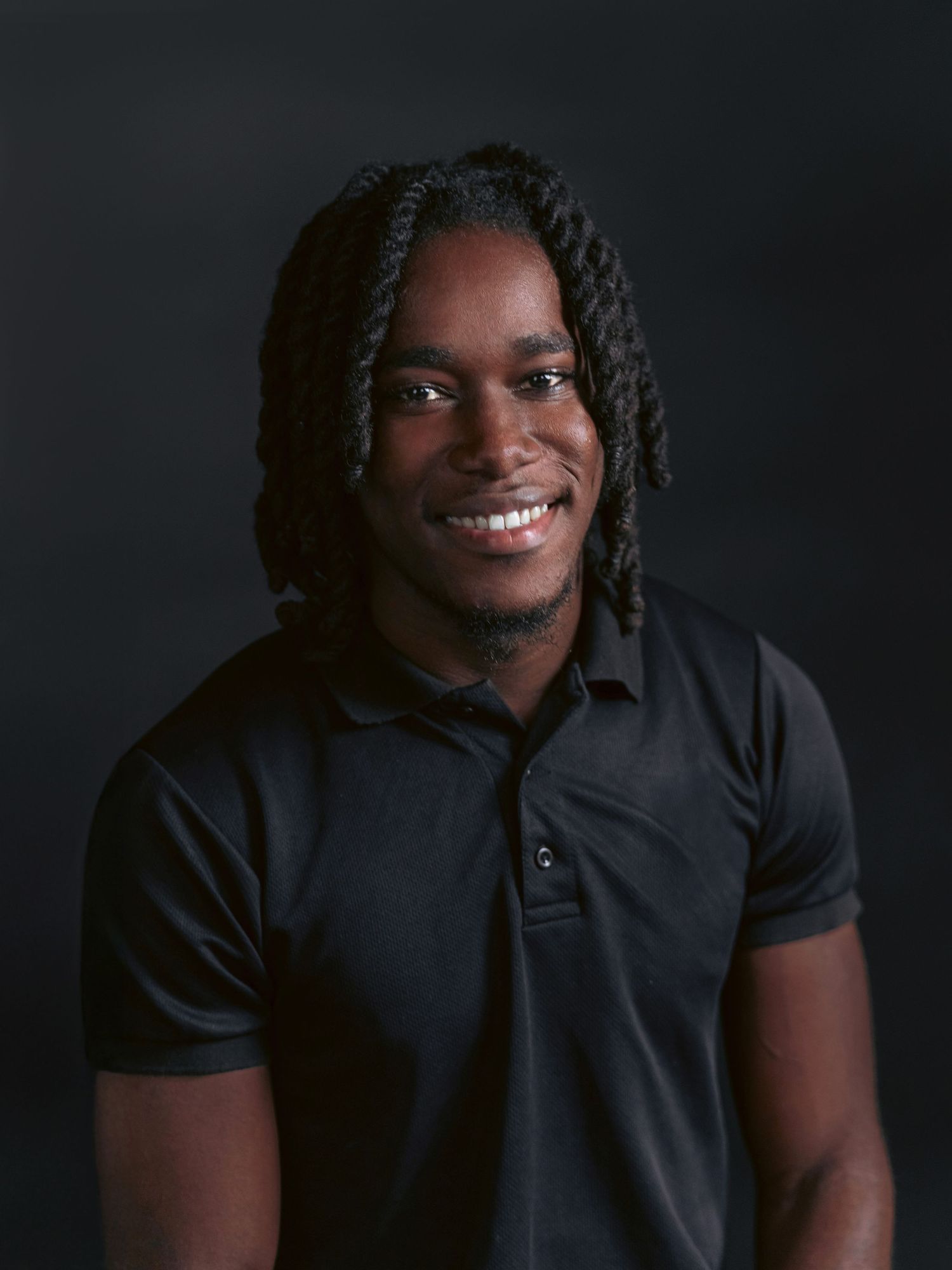 Zeshawn, owner of Captured by Bob, smiling in a studio portrait while wearing a black polo shirt against a dark background.