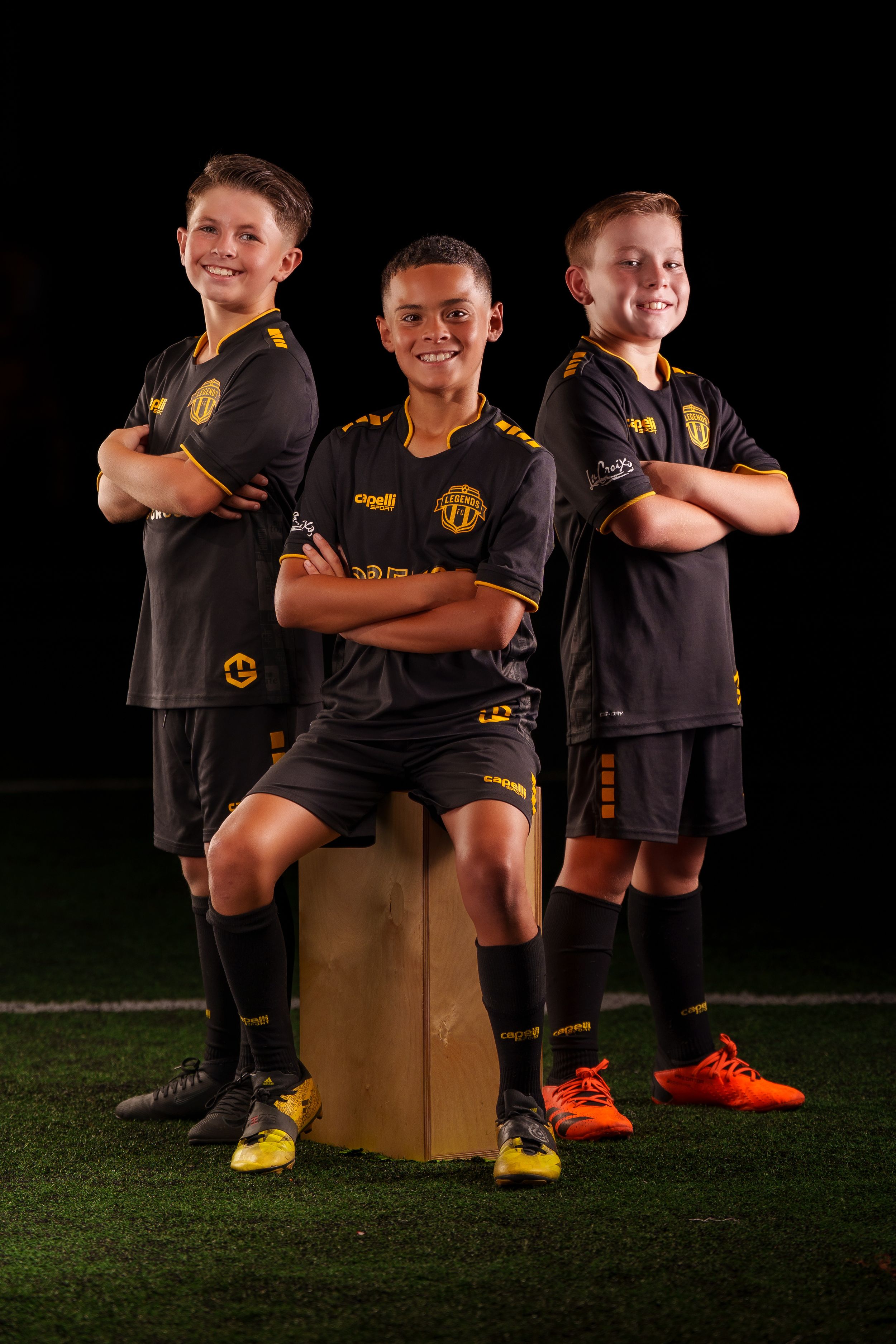 Youth soccer players in black uniforms pose together on a darkened field.