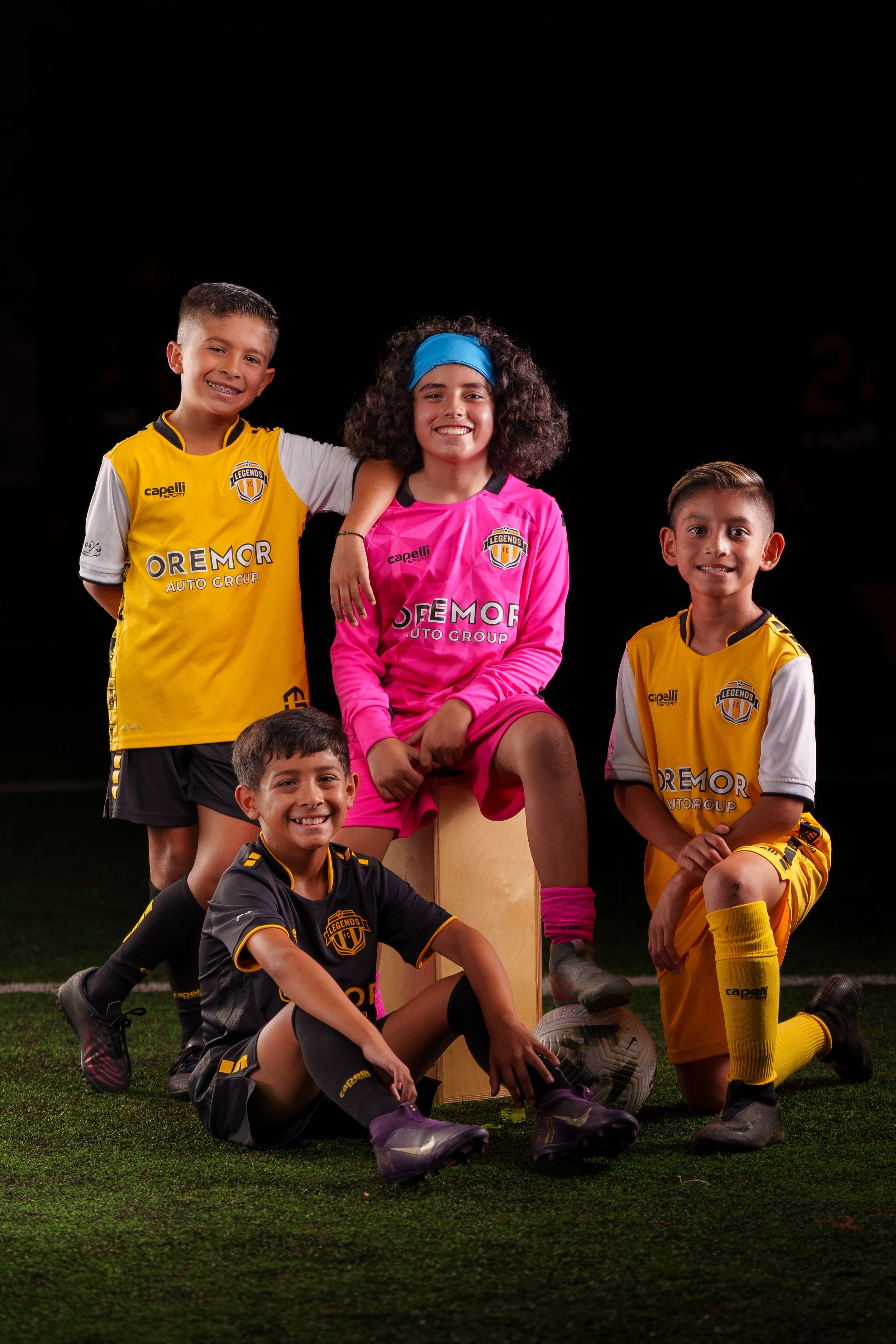 Soccer team members wearing yellow and pink jerseys gather for a group photo on grass.