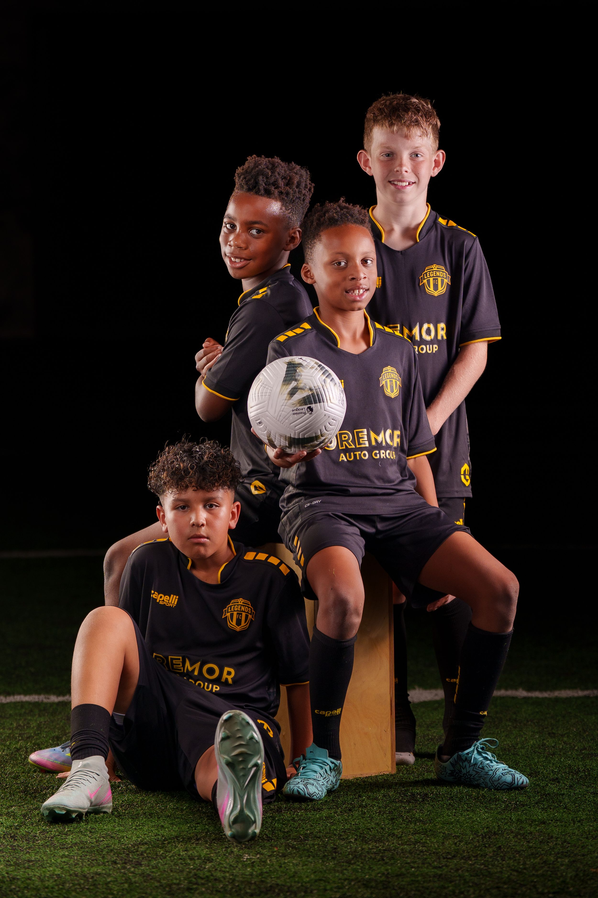 Youth athletes in dark uniforms sit casually on artificial turf for a team photo.