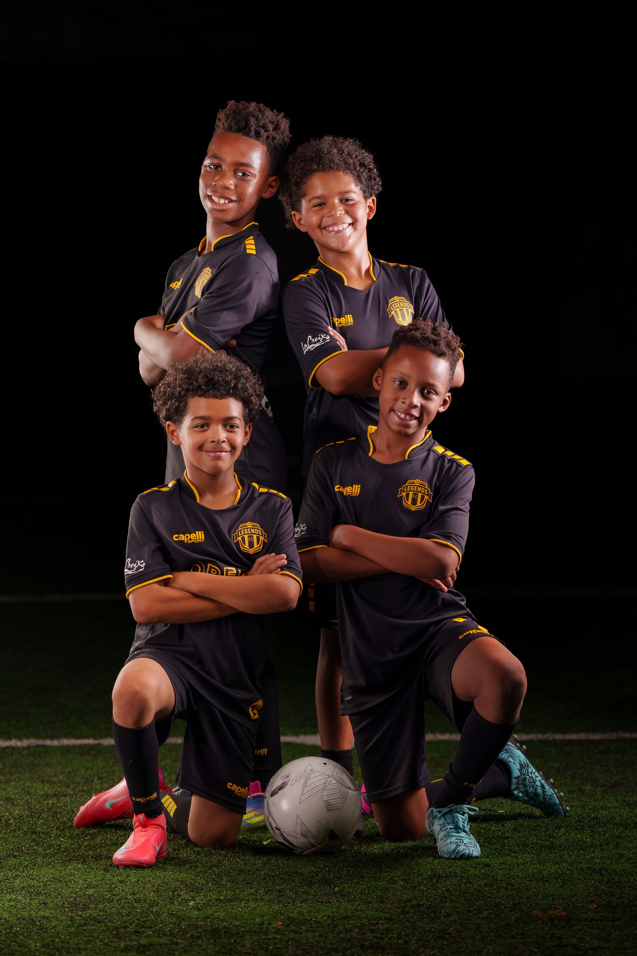 Group of young soccer players in dark uniforms pose together on a sports field.