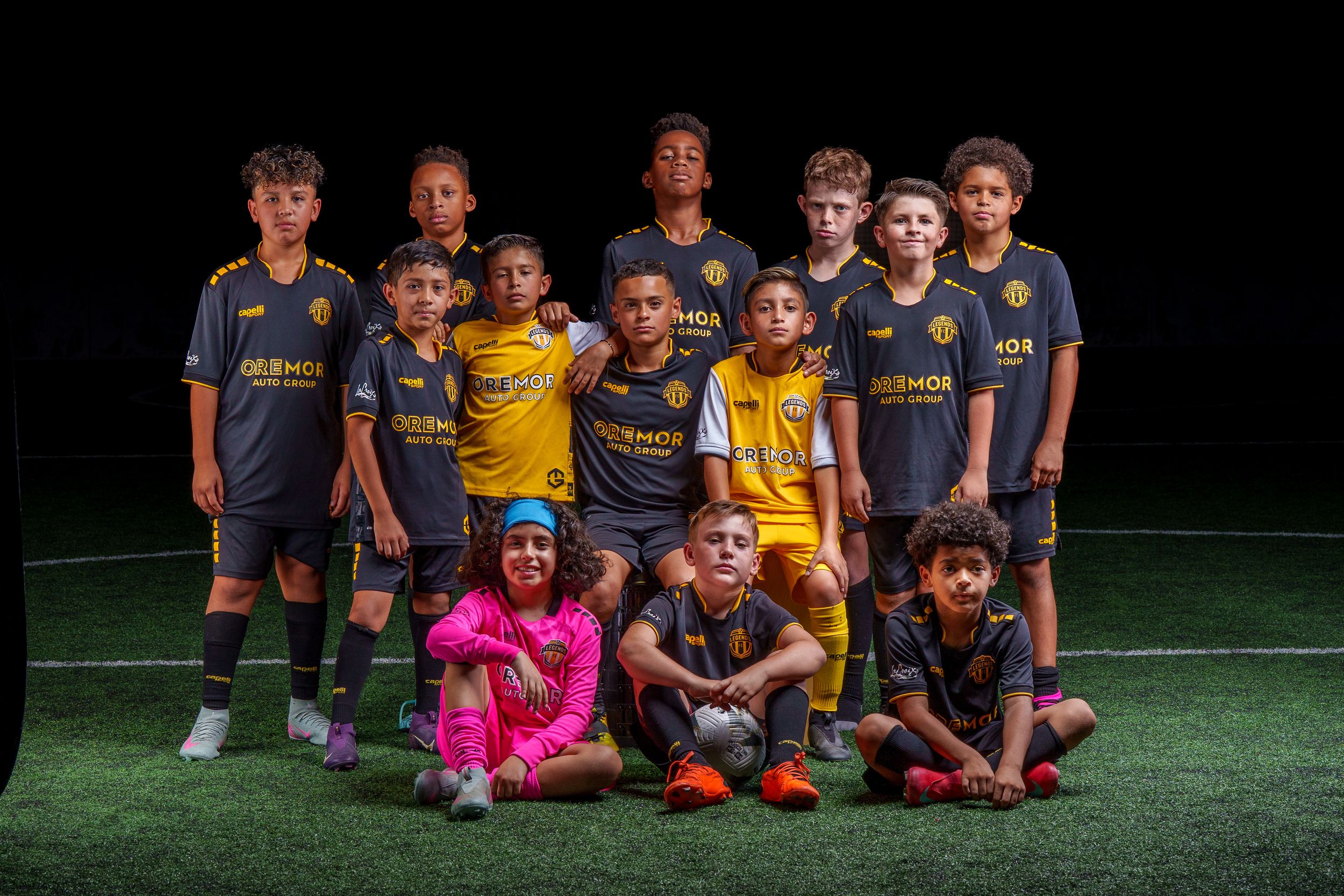 Large group of youth soccer players sitting together for a team photo on turf field.