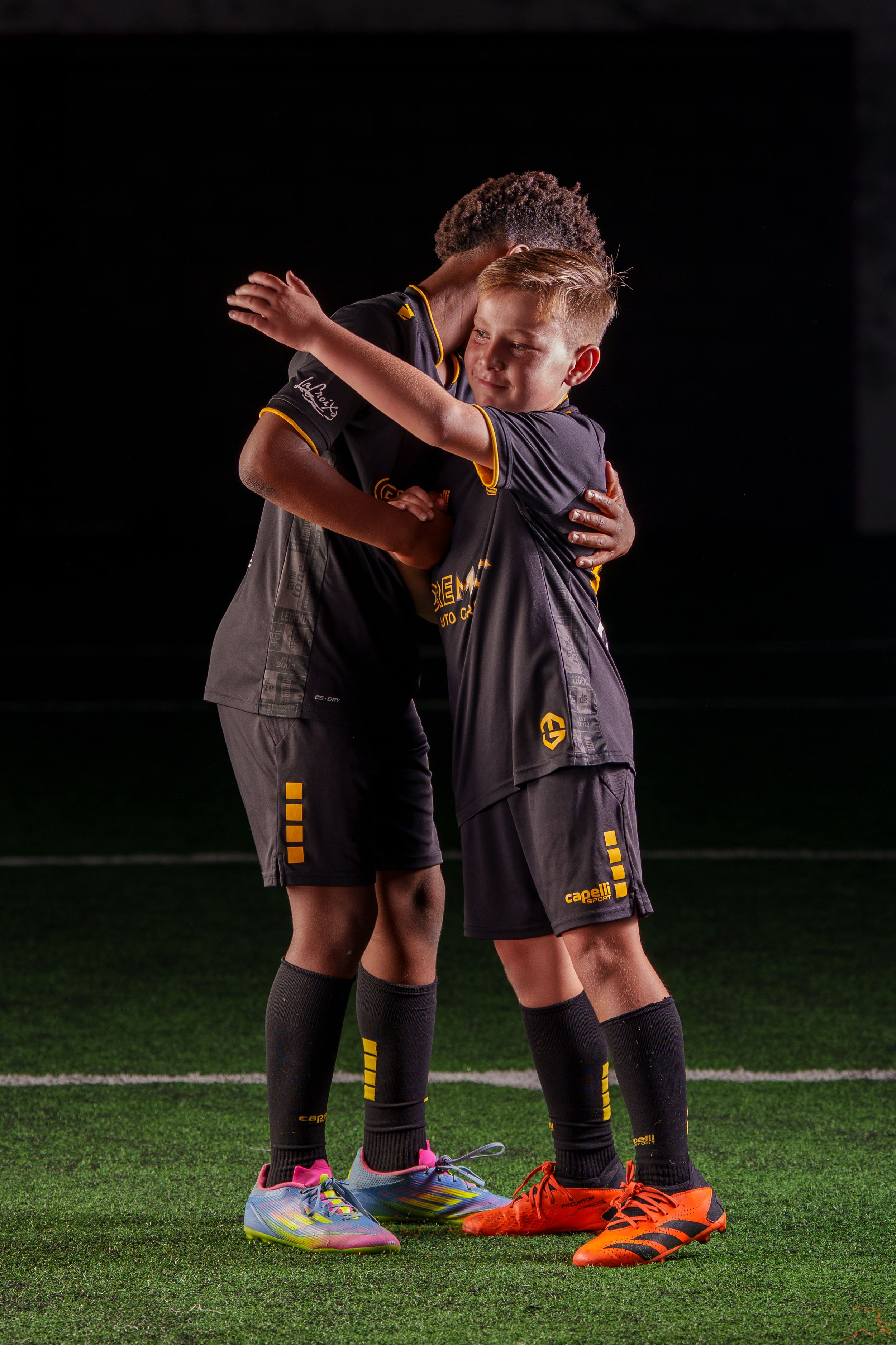 Cinematic photo of two youth soccer placers mid-embrace displaying camaraderie and friendship.